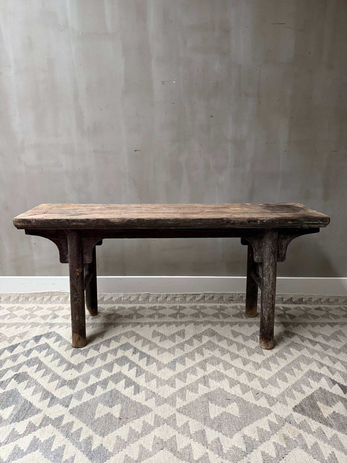 Authentiek handgemaakt houten bankje op een grijze vloerkleed in sober landelijk interieur