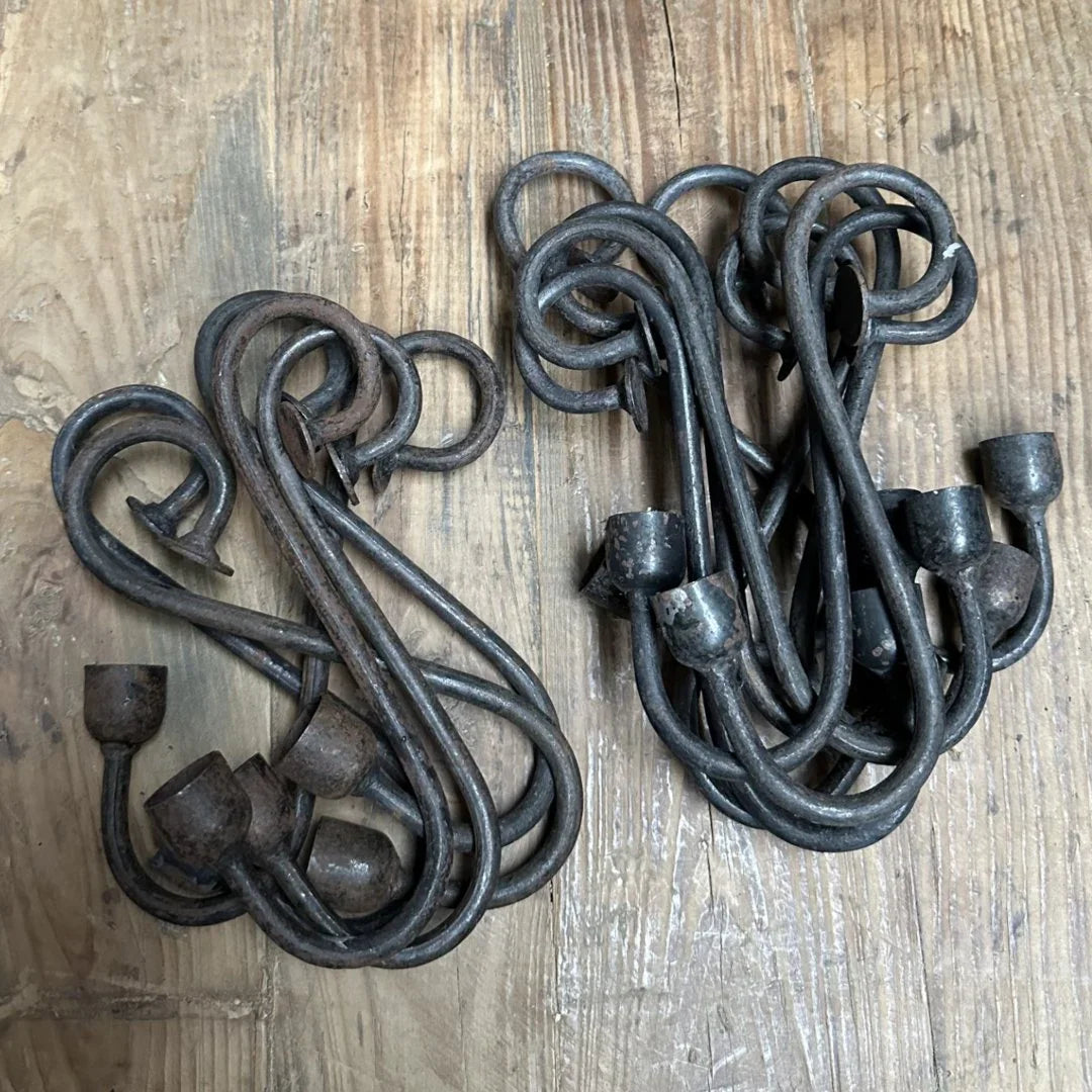 Twee bundels handgemaakte metalen glashaken op houten oppervlak, sober landelijk woonaccessoire.