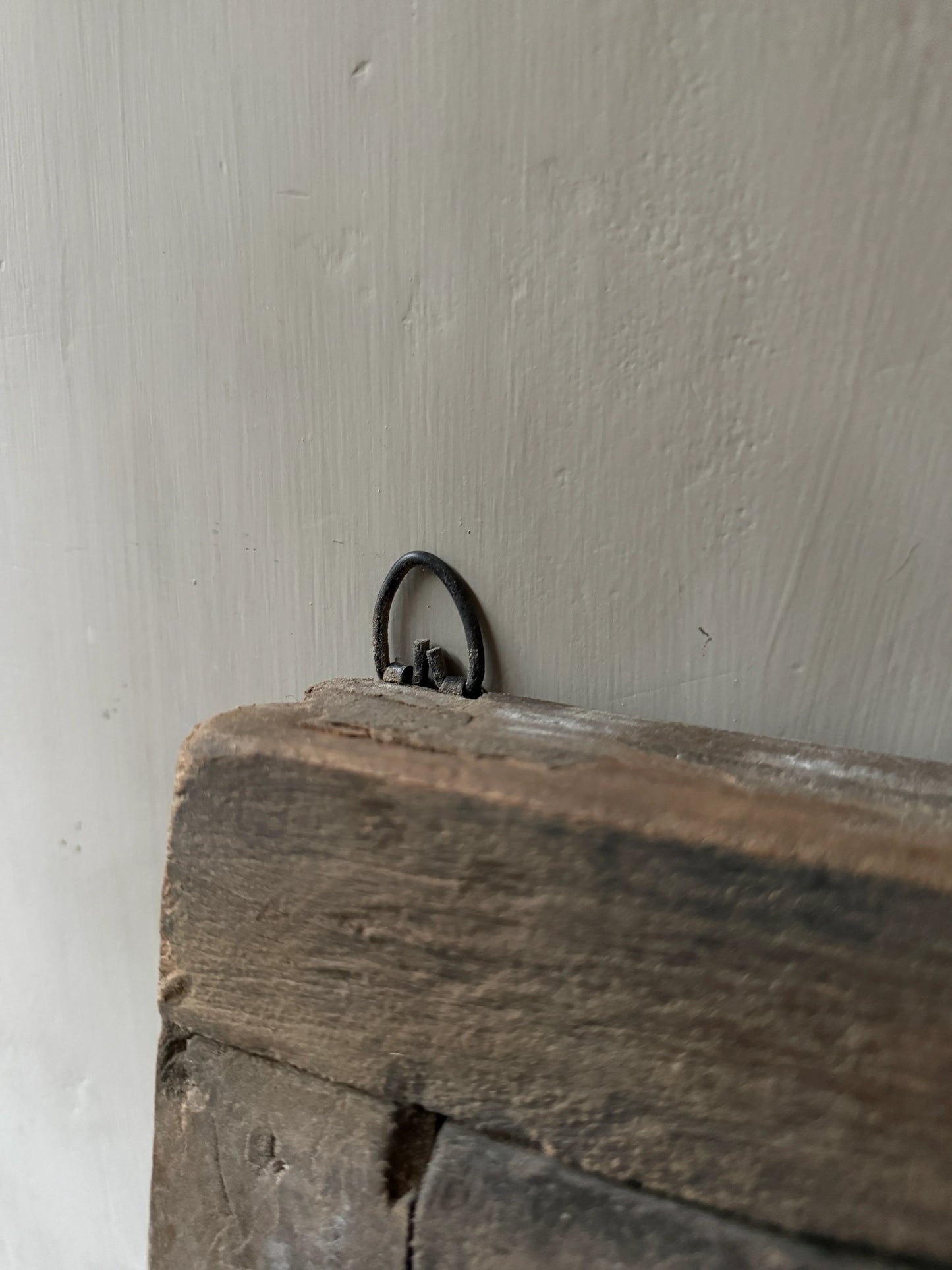 Detail van een authentiek handgemaakt houten luikje met metalen ophanglus, sober interieur