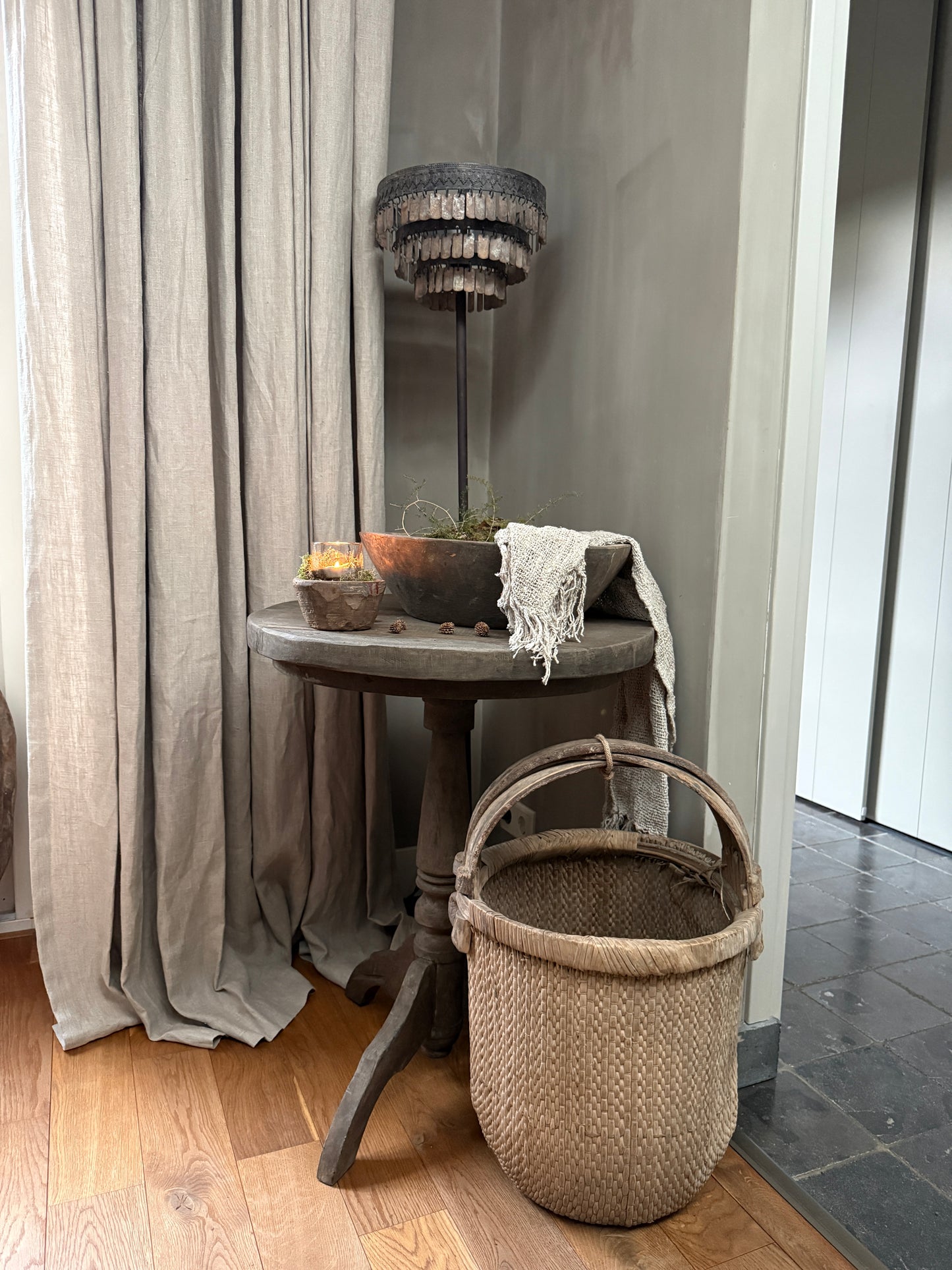 Landelijke houten tafel met handgemaakte mand, lamp en woonaccessoires in sober interieur