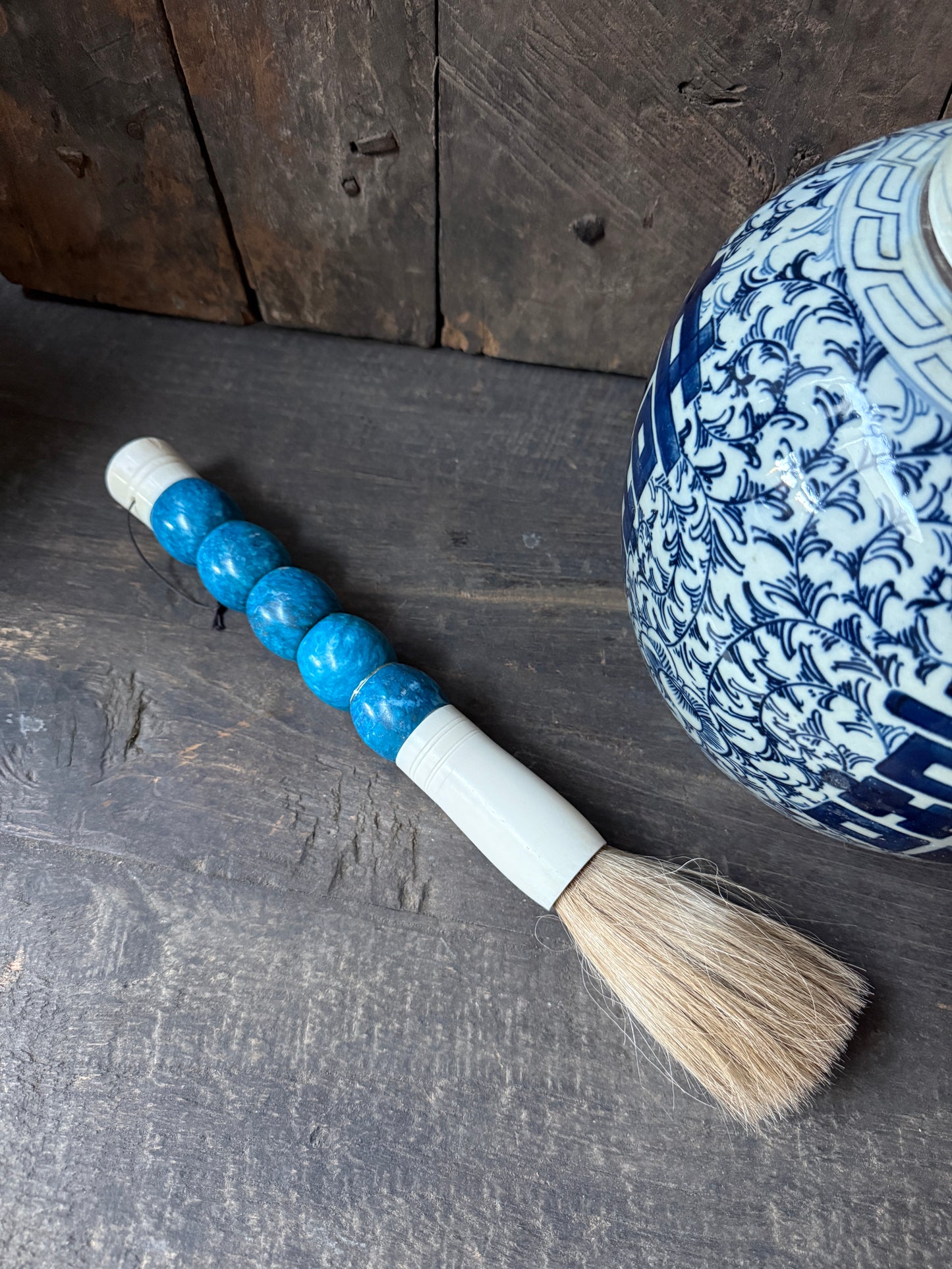 Handgemaakt penseel met blauwe kralen op houten tafel, naast oosters blauw-wit aardewerk, sober landelijk woonaccessoire