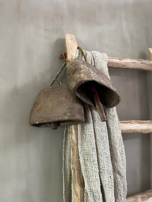 Oude metalen bel en linnen doek aan houten ladder, landelijke sobere woonaccessoire