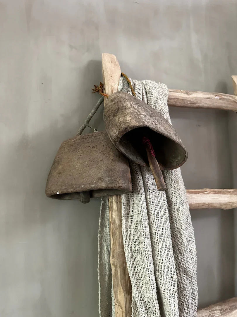 Oude metalen bel en linnen doek aan houten ladder, landelijke sobere woonaccessoire