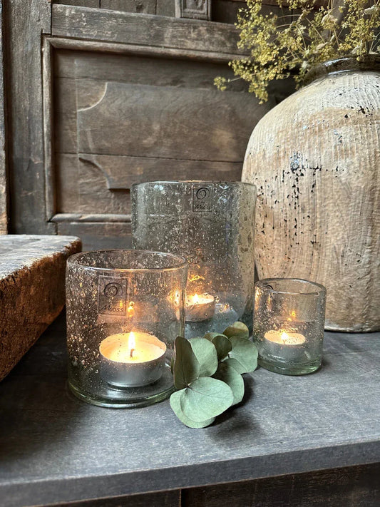 Handgemaakte glazen waxinelichthouders met brandende kaarsjes, sober landelijk interieur decoratie