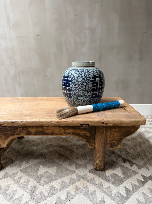 Authentieke antieke houten tafel met blauw-witte vaas en penseel, sober landelijk interieur