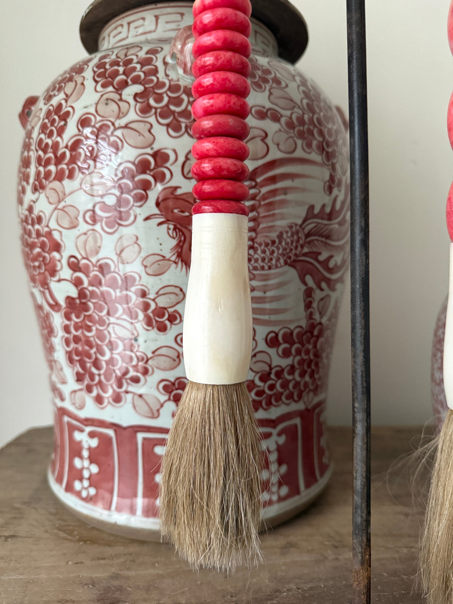 Handgemaakte kwast met roze kralen en vaas met rood-wit patroon, landelijk interieur