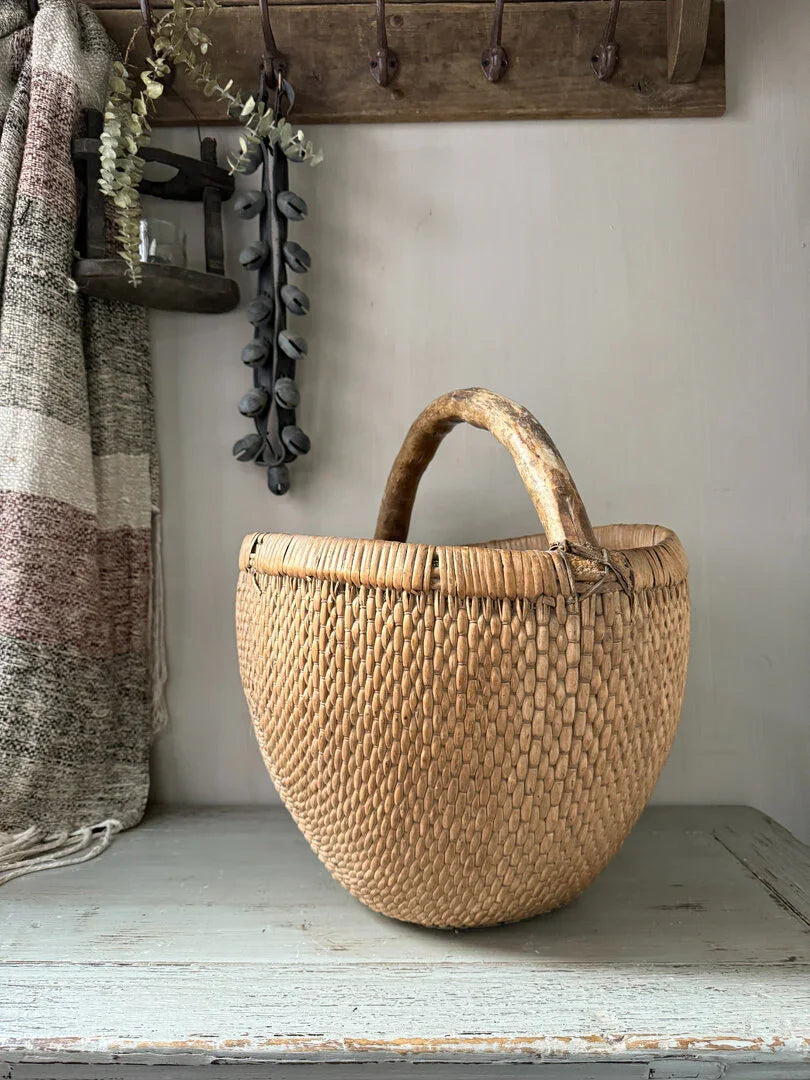 Handgemaakte plukmand met houten handvat op een landelijke houten plank, sober interieur