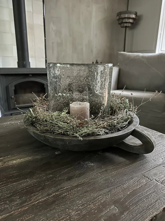 Houten schaal met handvat, gevuld met decoratief mos, windlicht en kaars op houten tafel in landelijk sober interieur