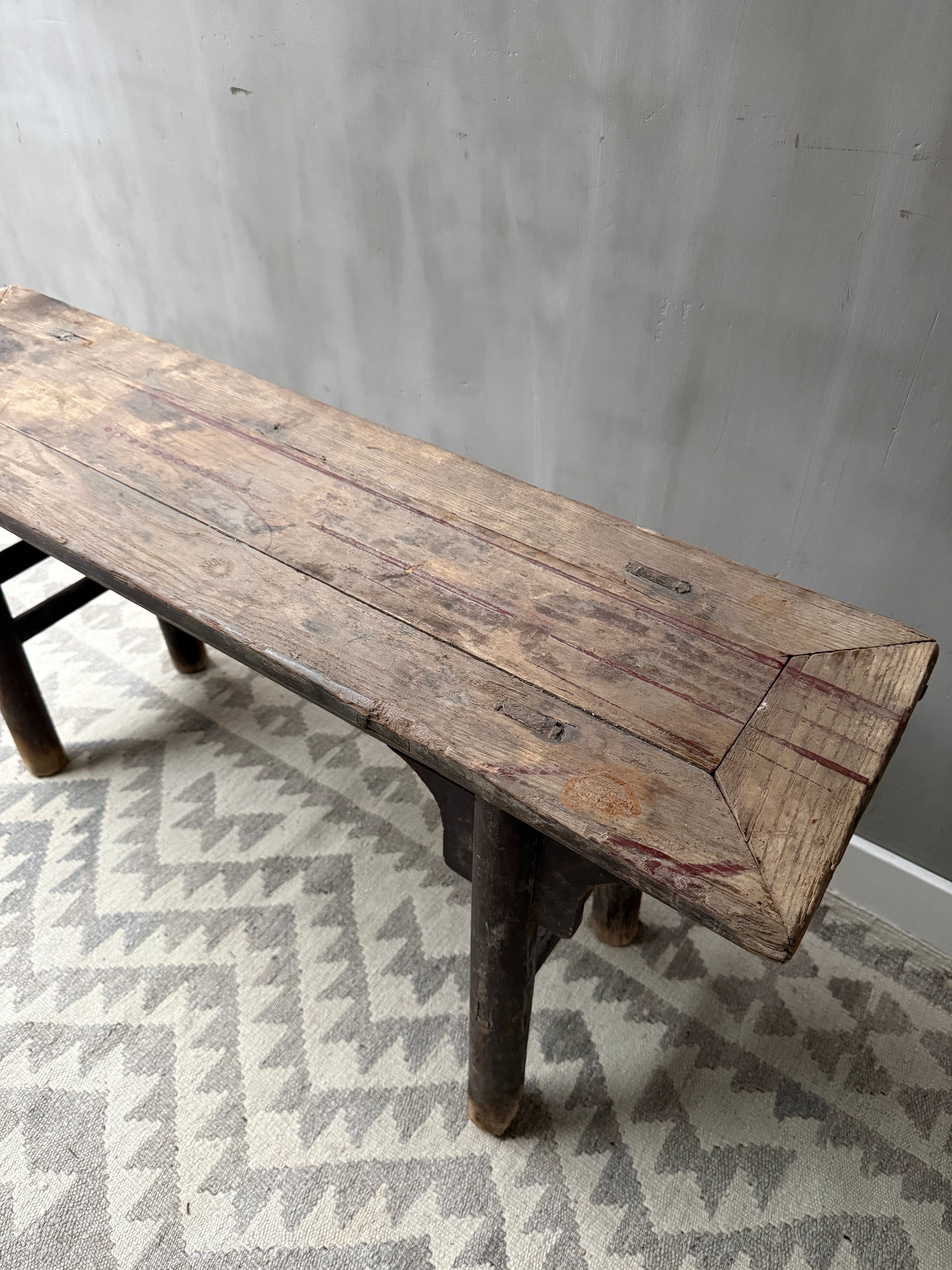 Authentiek handgemaakt houten bankje met verweerd oppervlak op zigzag vloerkleed, sober interieur