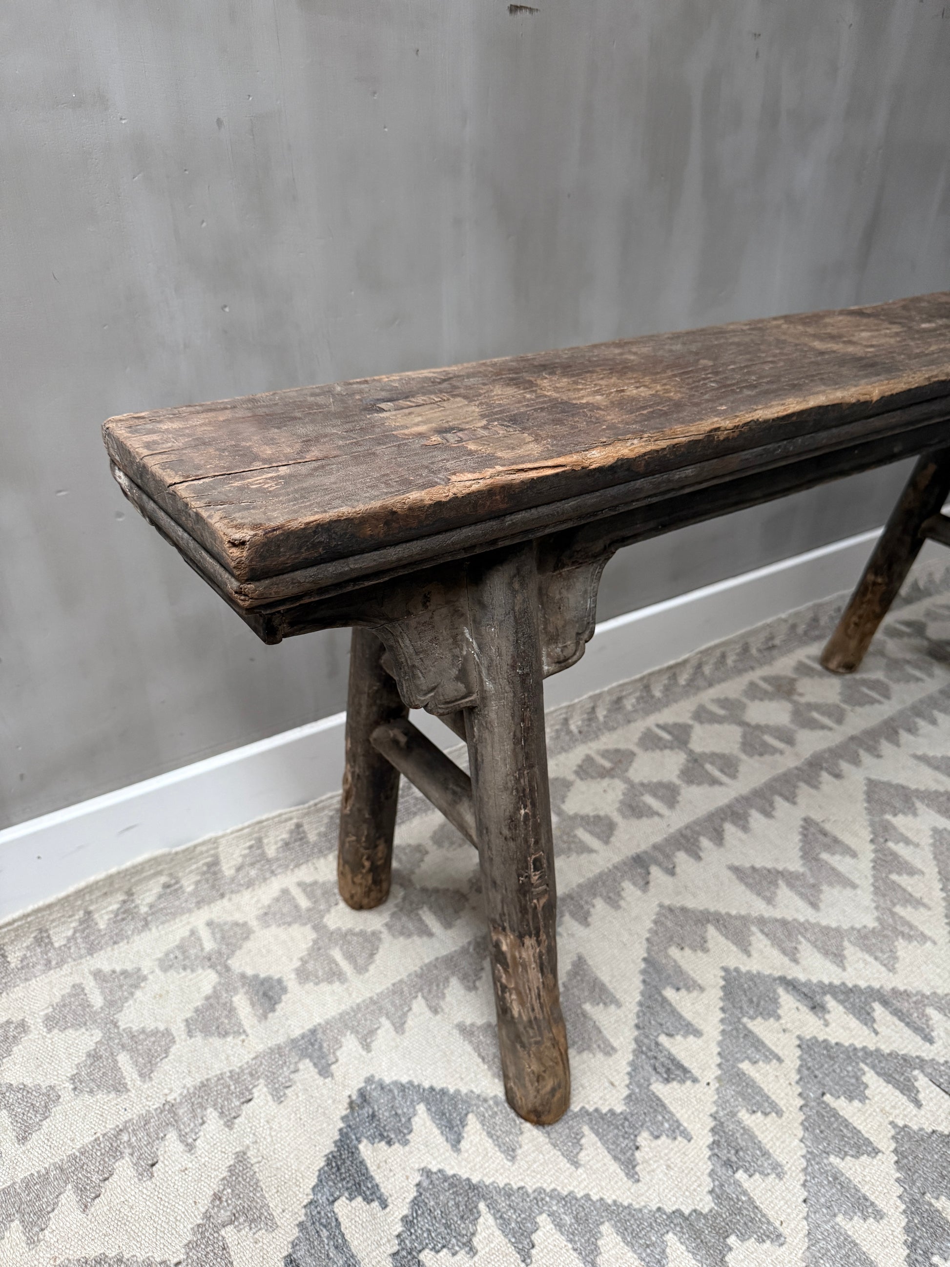 Authentiek, handgemaakt houten bankje op etnisch vloerkleed, sober landelijk interieur