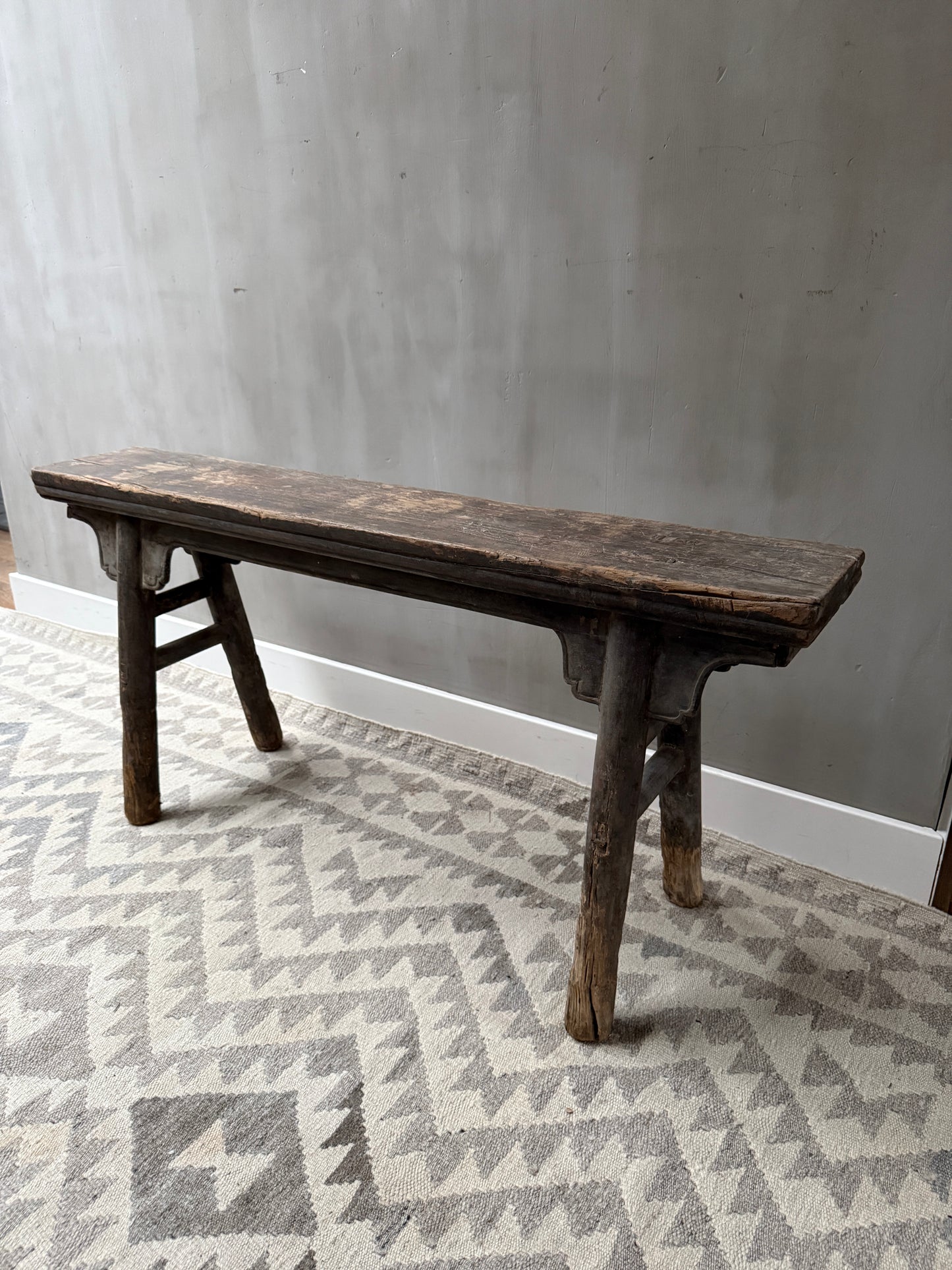 Authentiek handgemaakt houten bankje op een licht vloerkleed, landelijk sober interieur