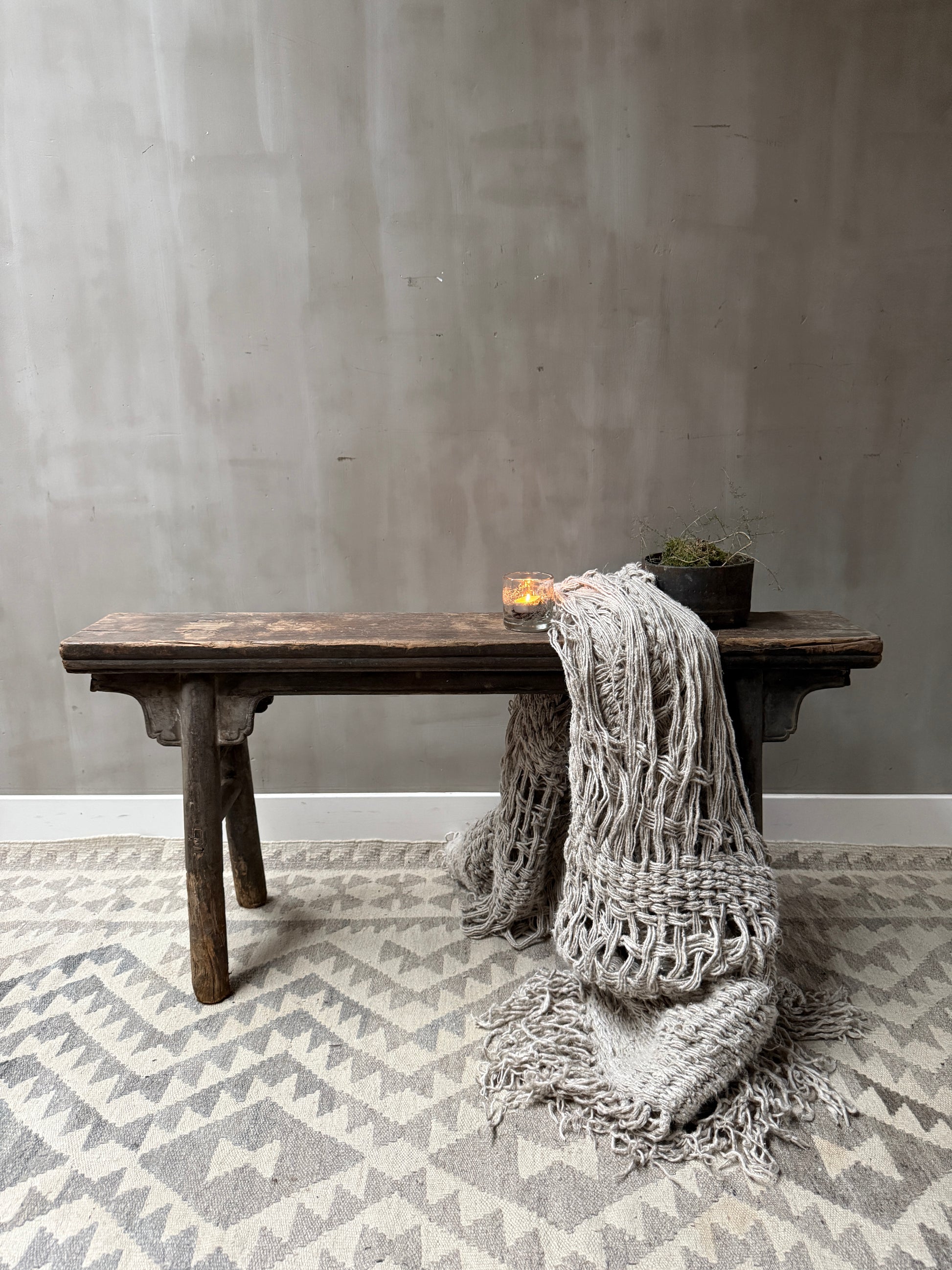 Handgemaakt houten bankje met grof gebreid plaid, kaarsje en plant, landelijk sober interieur