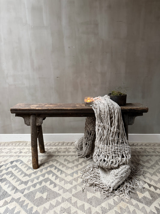 Handgemaakt houten bankje met grof gebreid plaid, kaarsje en plant, landelijk sober interieur