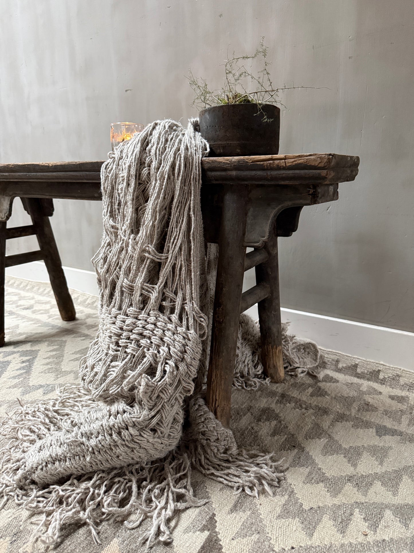 Landelijk houten bankje met handgemaakte plaid, plant en kaarsje, sober interieur