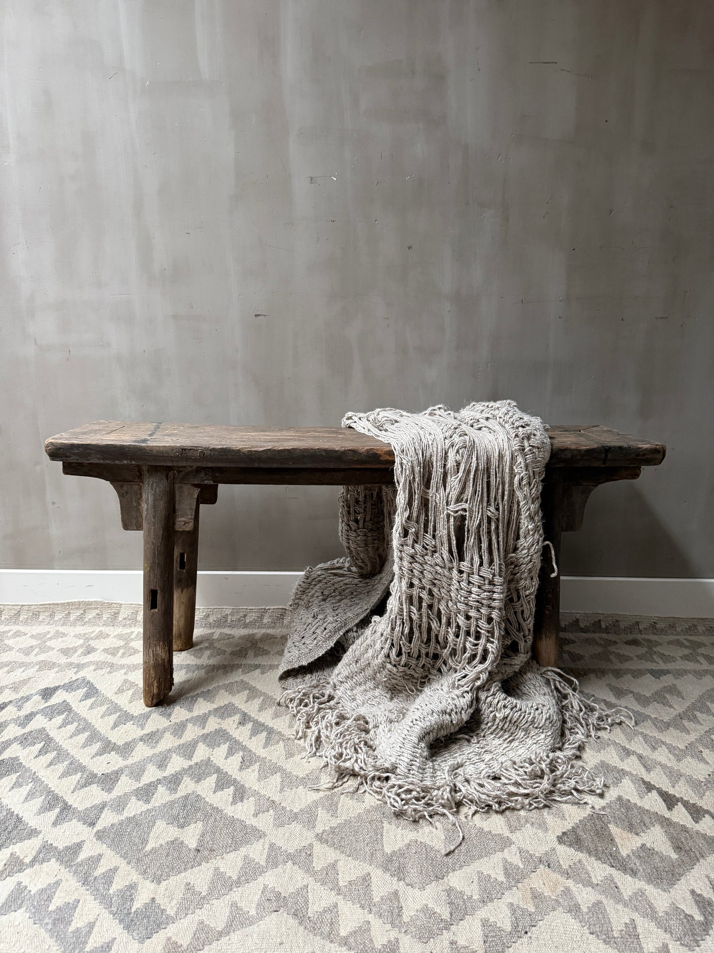 Authentiek houten bankje met grof gebreide plaid op vloerkleed, landelijk sober interieur