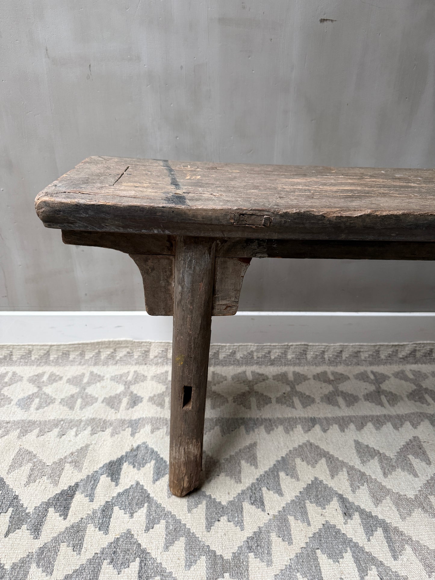 Authentiek houten bankje op een lichtgrijs vloerkleed, landelijk en sober interieur