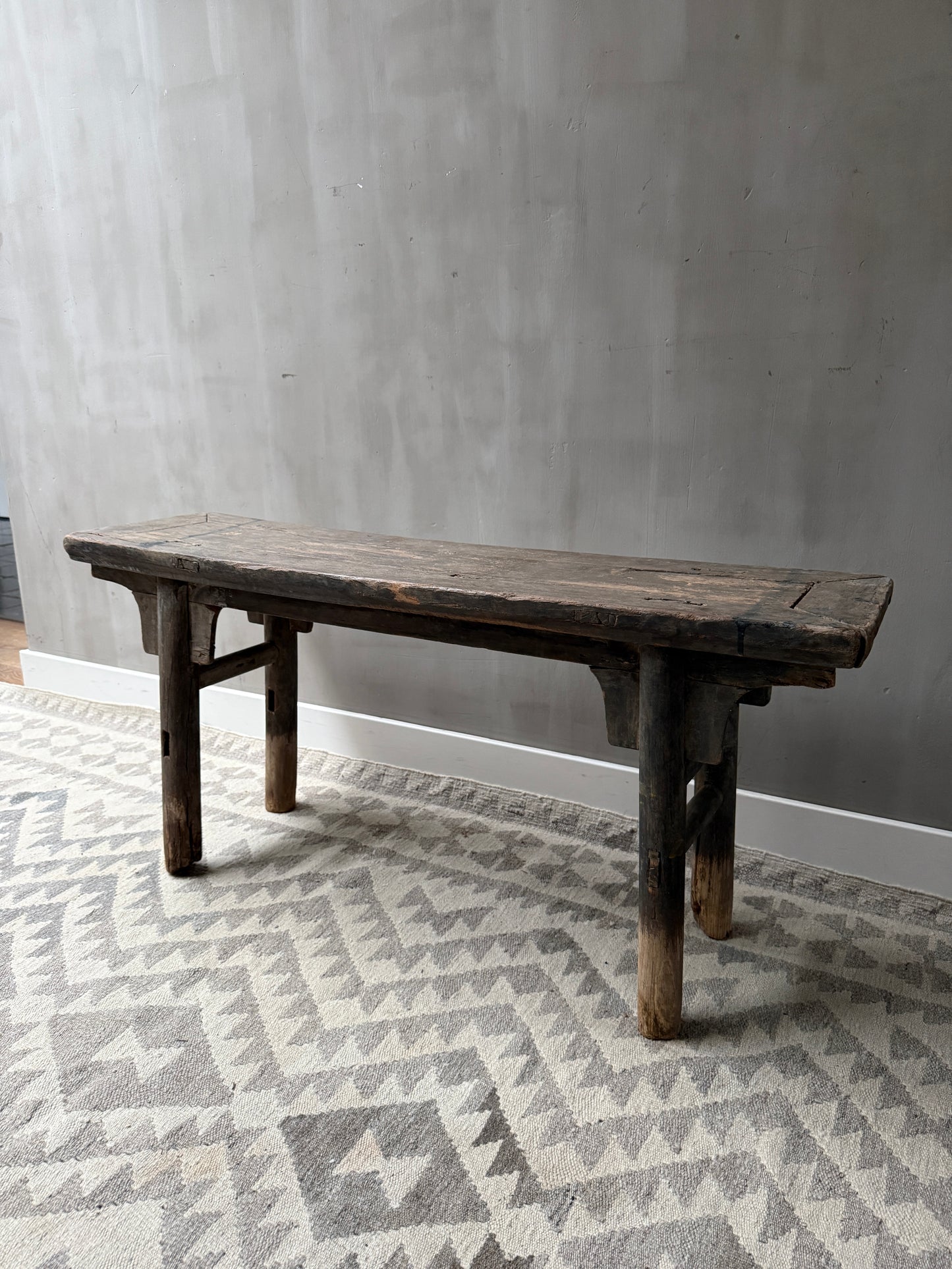 Authentiek, handgemaakt houten bankje op licht vloerkleed, sober landelijk interieur