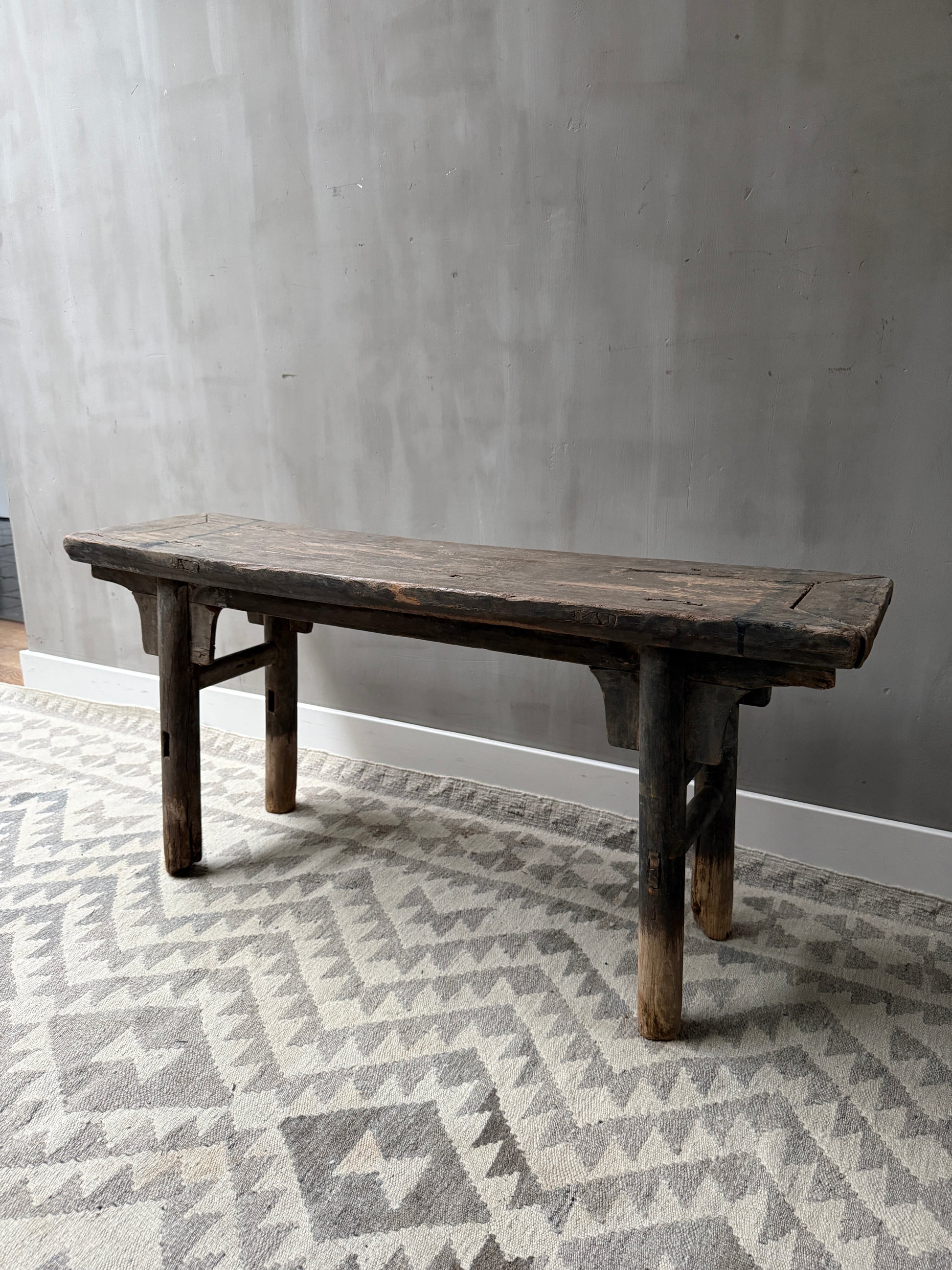 Authentiek, handgemaakt houten bankje op licht vloerkleed, sober landelijk interieur