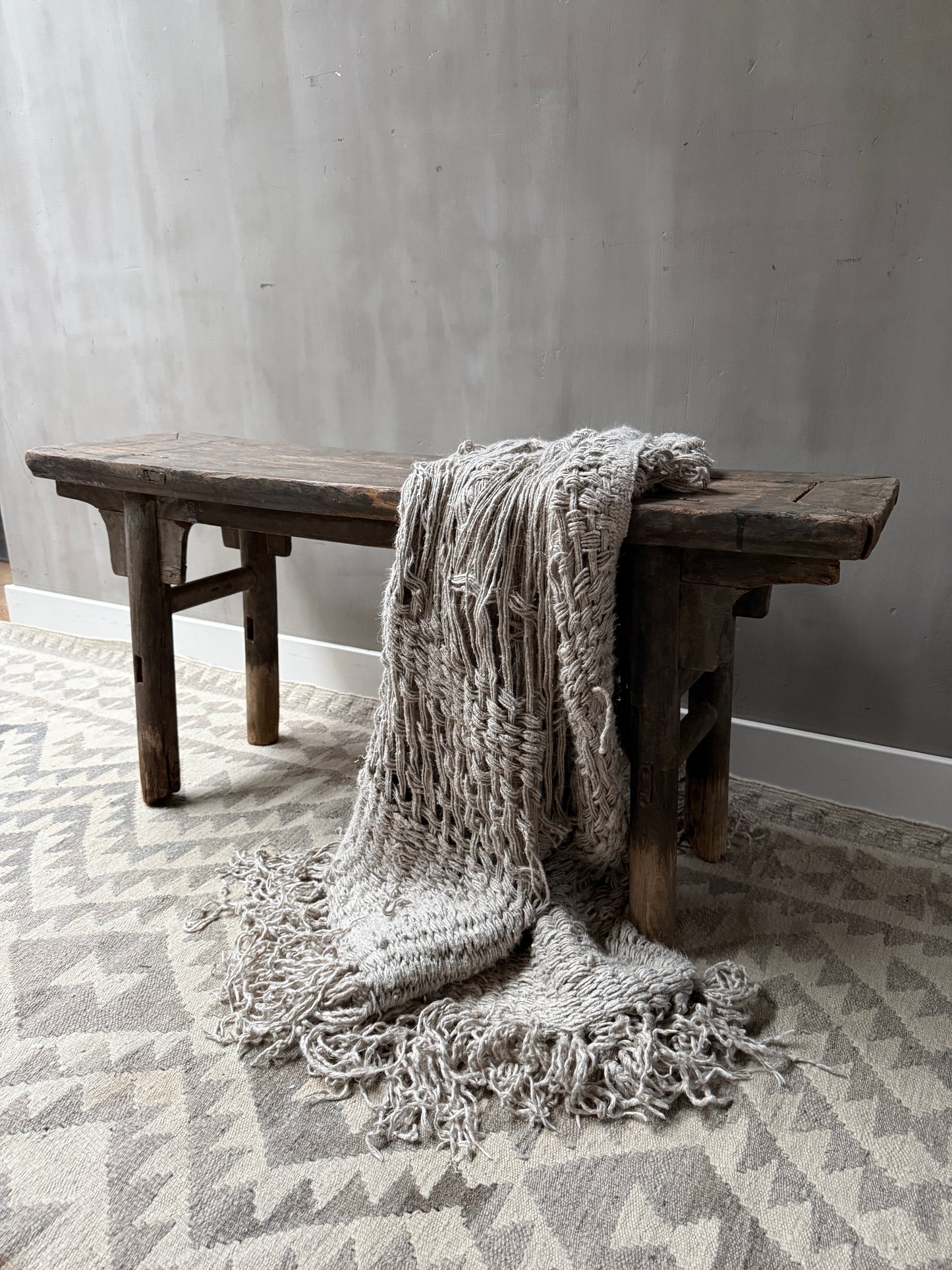 Authentiek houten bankje met grofgebreide plaid op landelijk vloerkleed, sober interieur