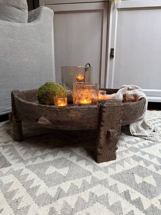 Houten chakkitafel met handgemaakte windlichten en mosbal op een sober, landelijk vloerkleed