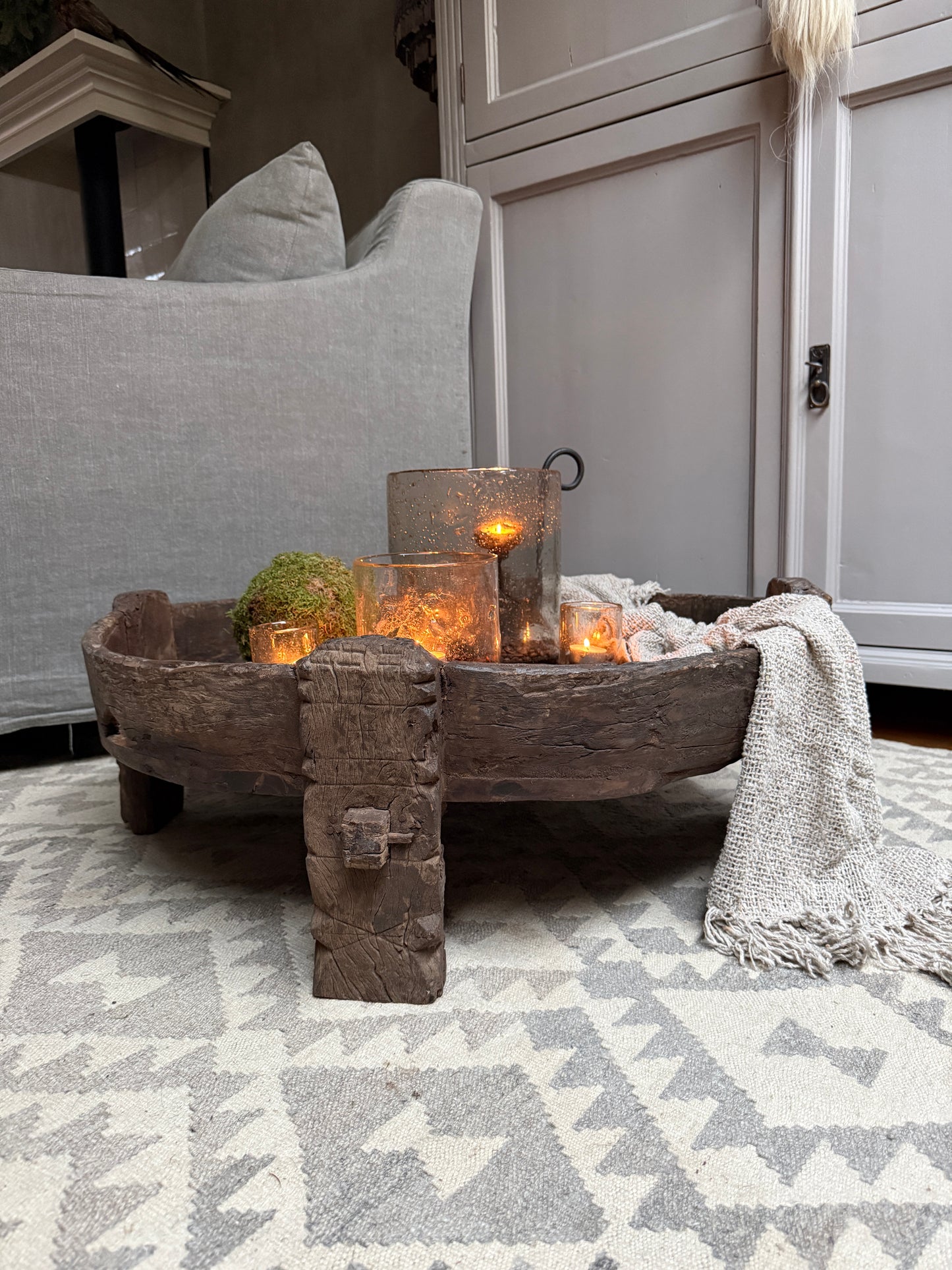 Authentieke houten chakkitafel met glaslichten en plaids, landelijk sober interieur.