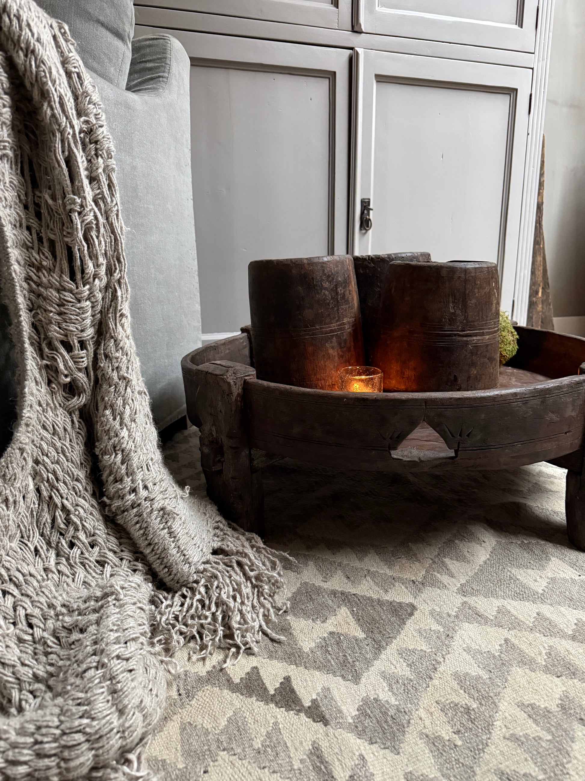 Landelijke houten chakkitafel met kaars, plaid en vintage accessoires in sober interieur