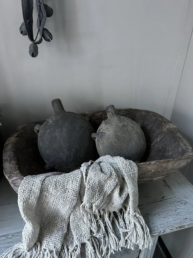 Handgemaakte Chinese oliefles in een houten schaal met grof gebreid plaid, sober landelijk interieur