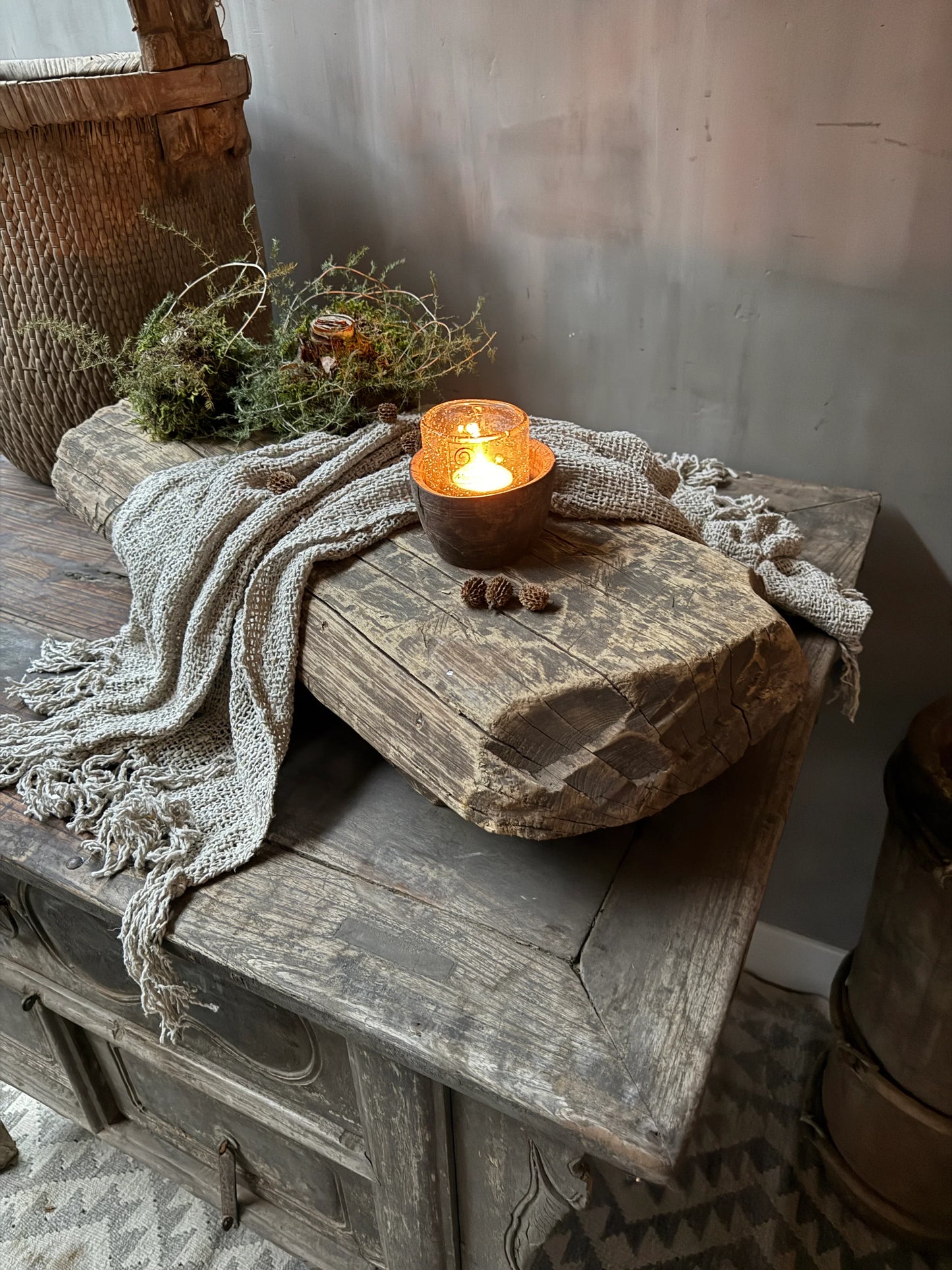 Authentieke houten side table met kaars, groendecoratie en linnen plaid in sober landelijk interieur