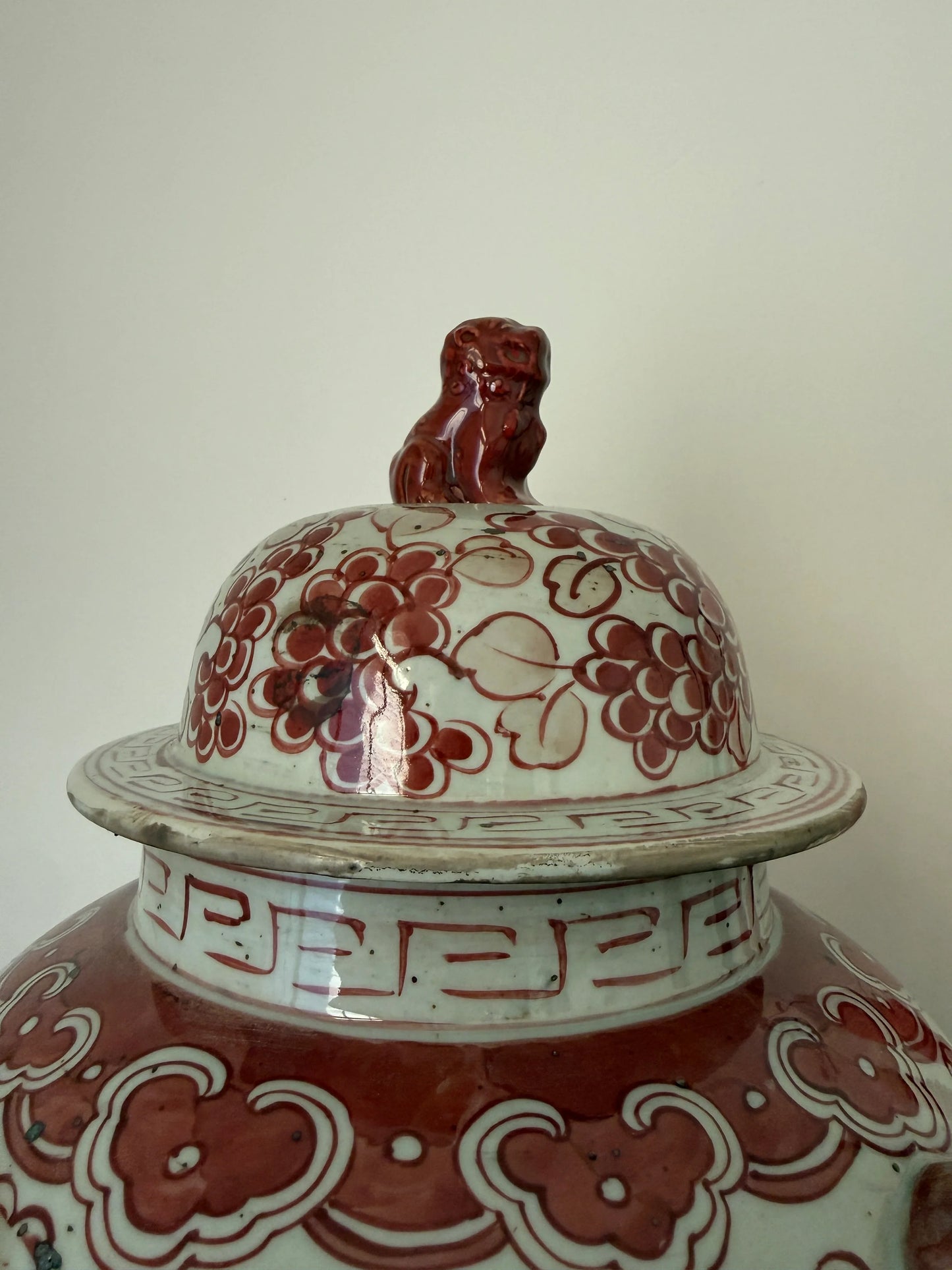 Handgemaakte keramische pot met rood bloemmotief en leeuw op deksel, sober landelijk interieur