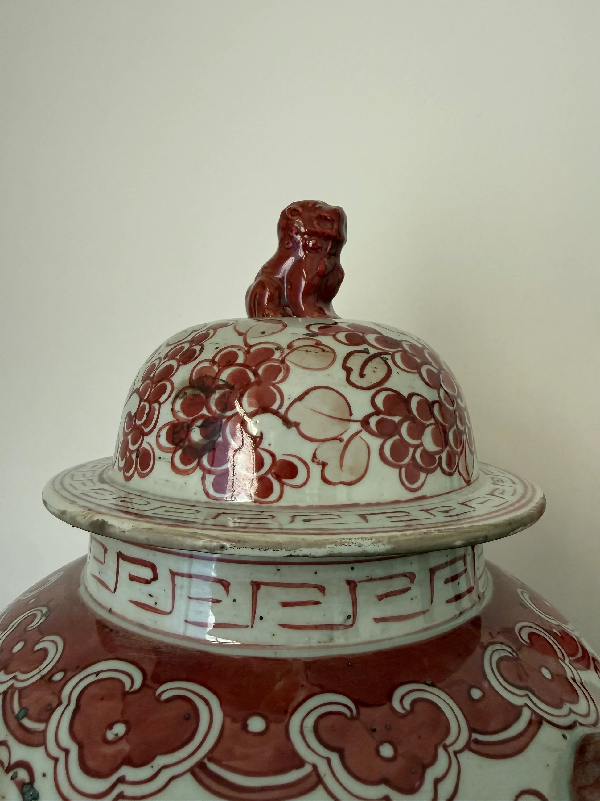 Handgemaakte keramische pot met rood bloemmotief en leeuw op deksel, sober landelijk interieur