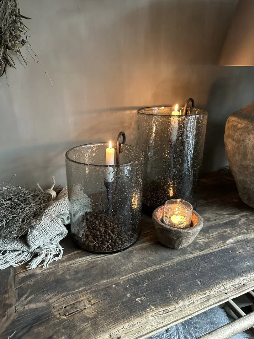 Handgemaakte glazen windlichten met brandende kaarsen op robuuste houten tafel, landelijk interieur