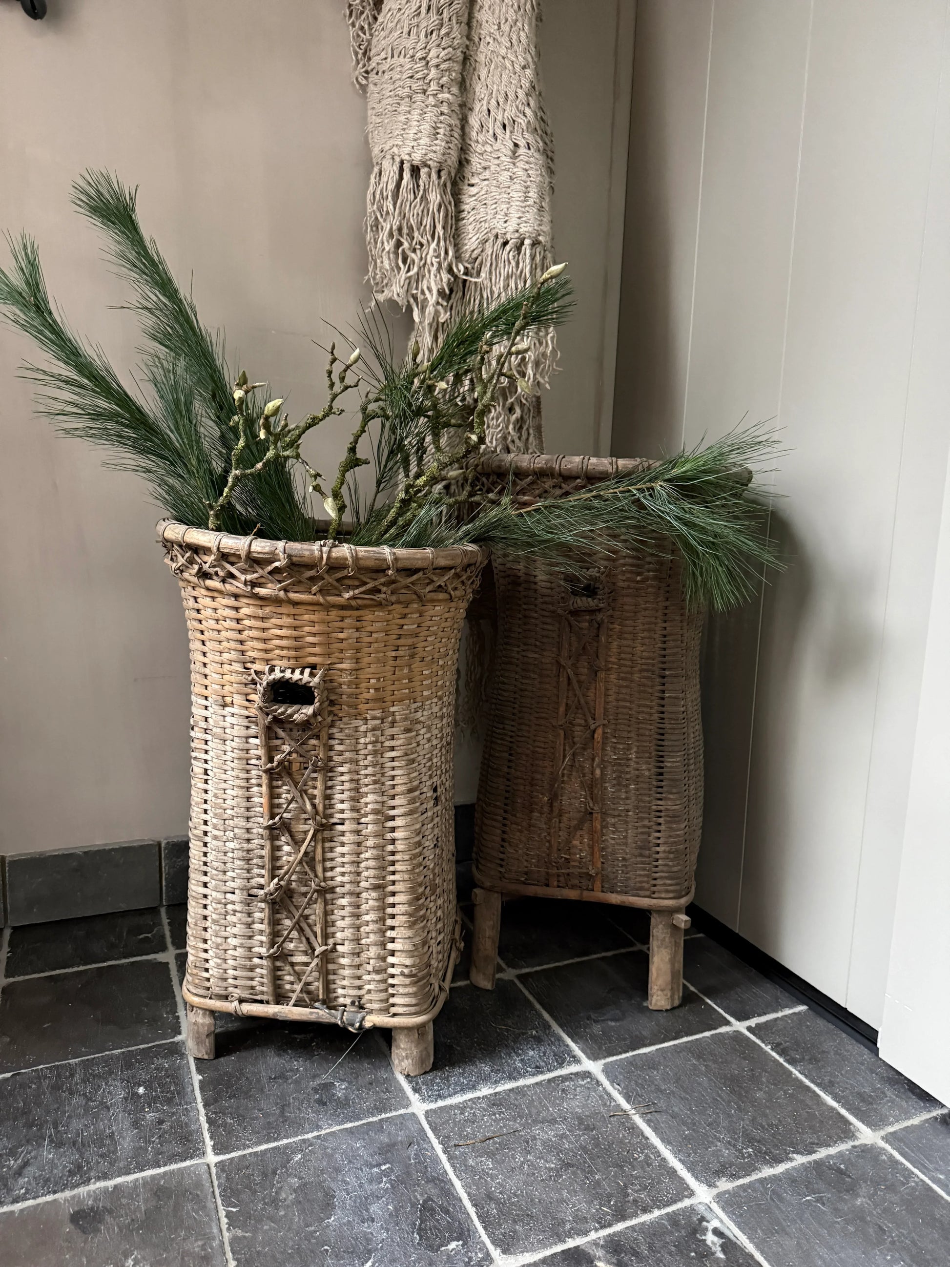 Authentieke handgemaakte hoge manden met dennentakken op natuurstenen vloer, landelijk interieur