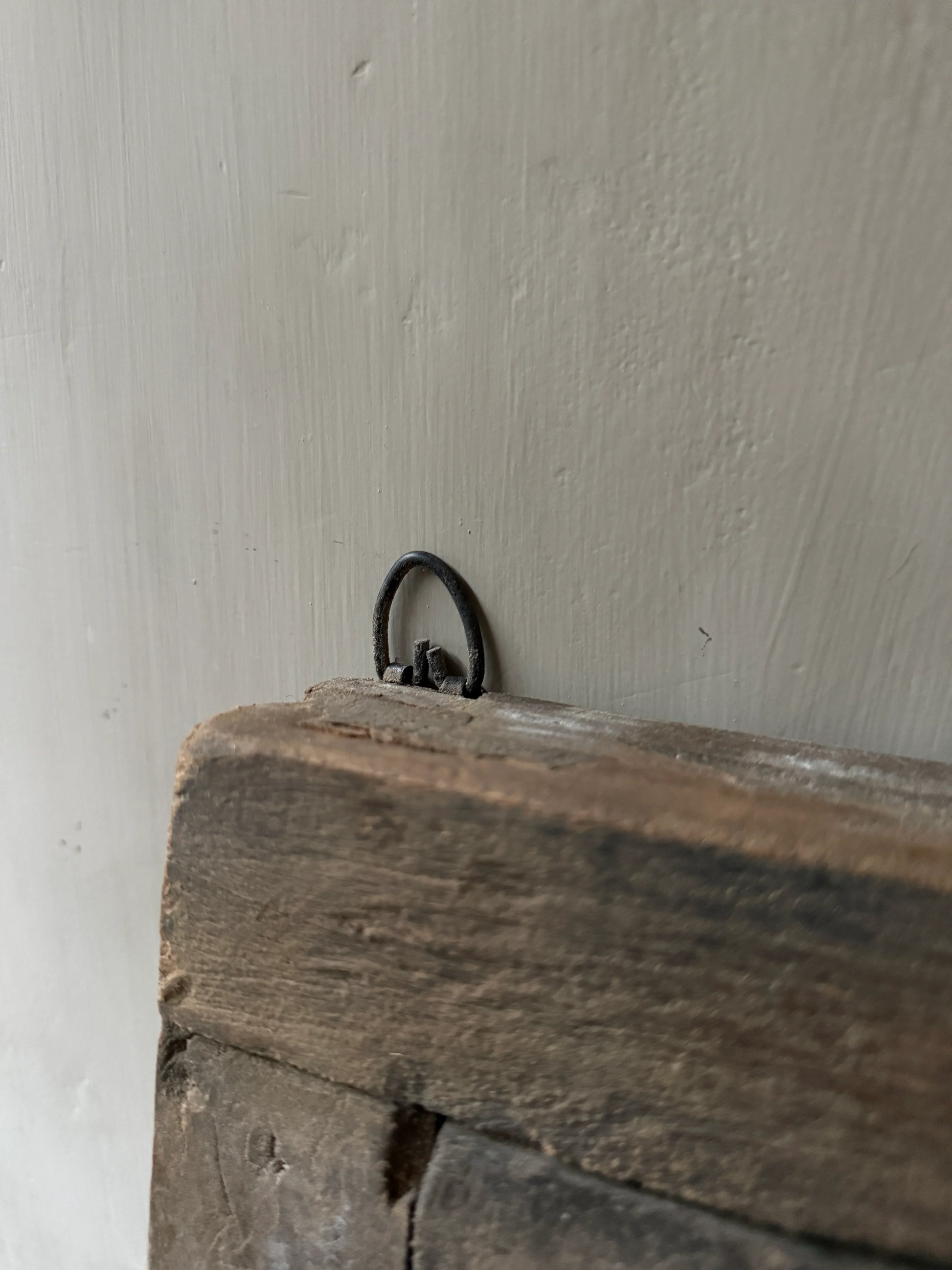 Detail van een authentiek handgemaakt houten luikje met metalen ophanglus, sober interieur