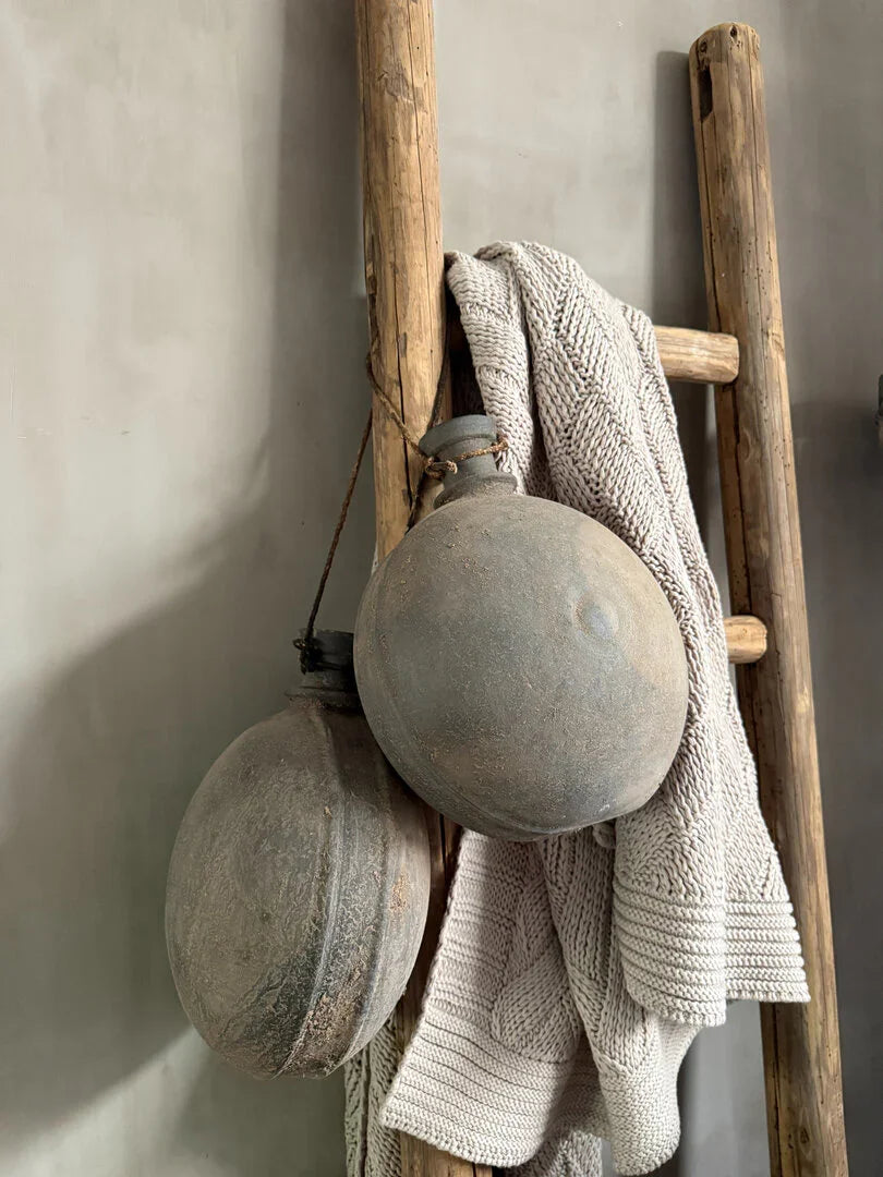 Houten ladder met handgemaakt plaid en originele waterkruiken, sober landelijk interieur