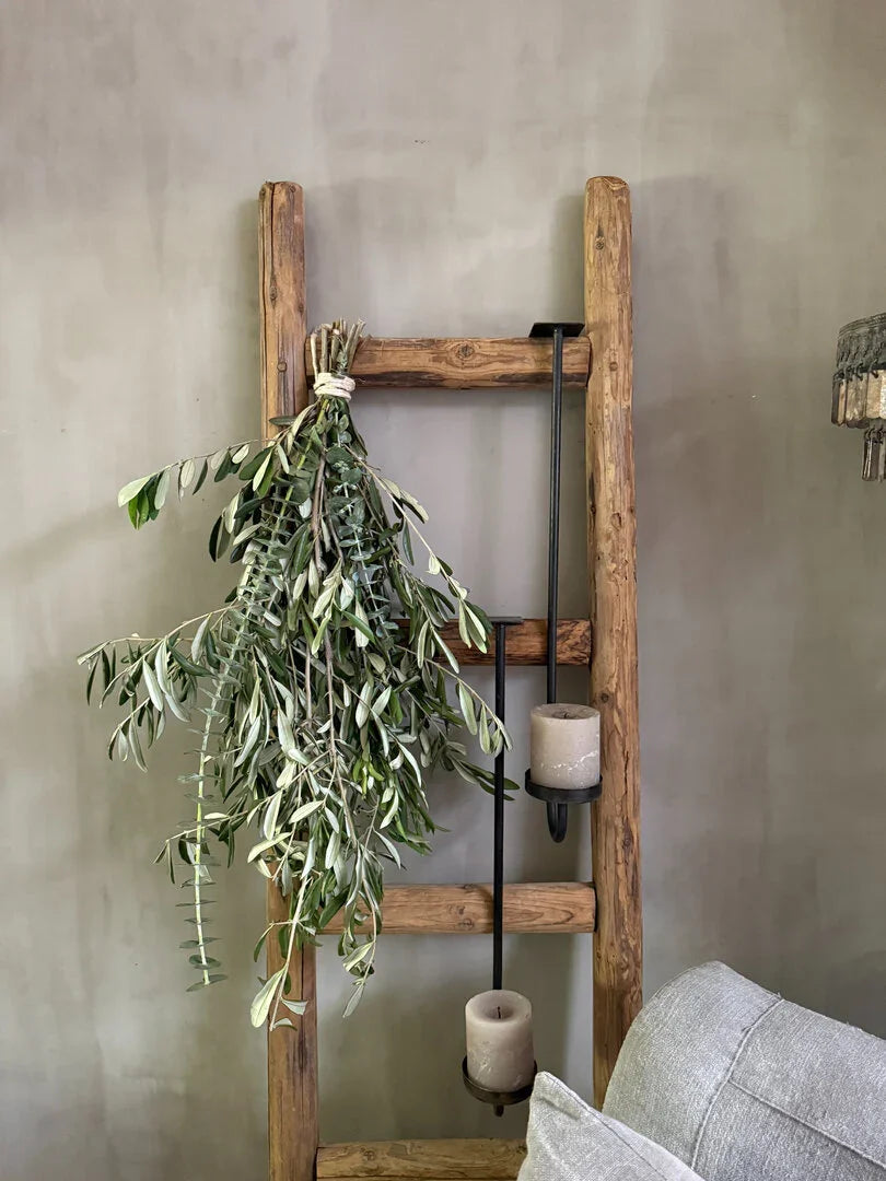 Houten ladder met groene tak en landelijke kaarshouders aan muur, sober interieur