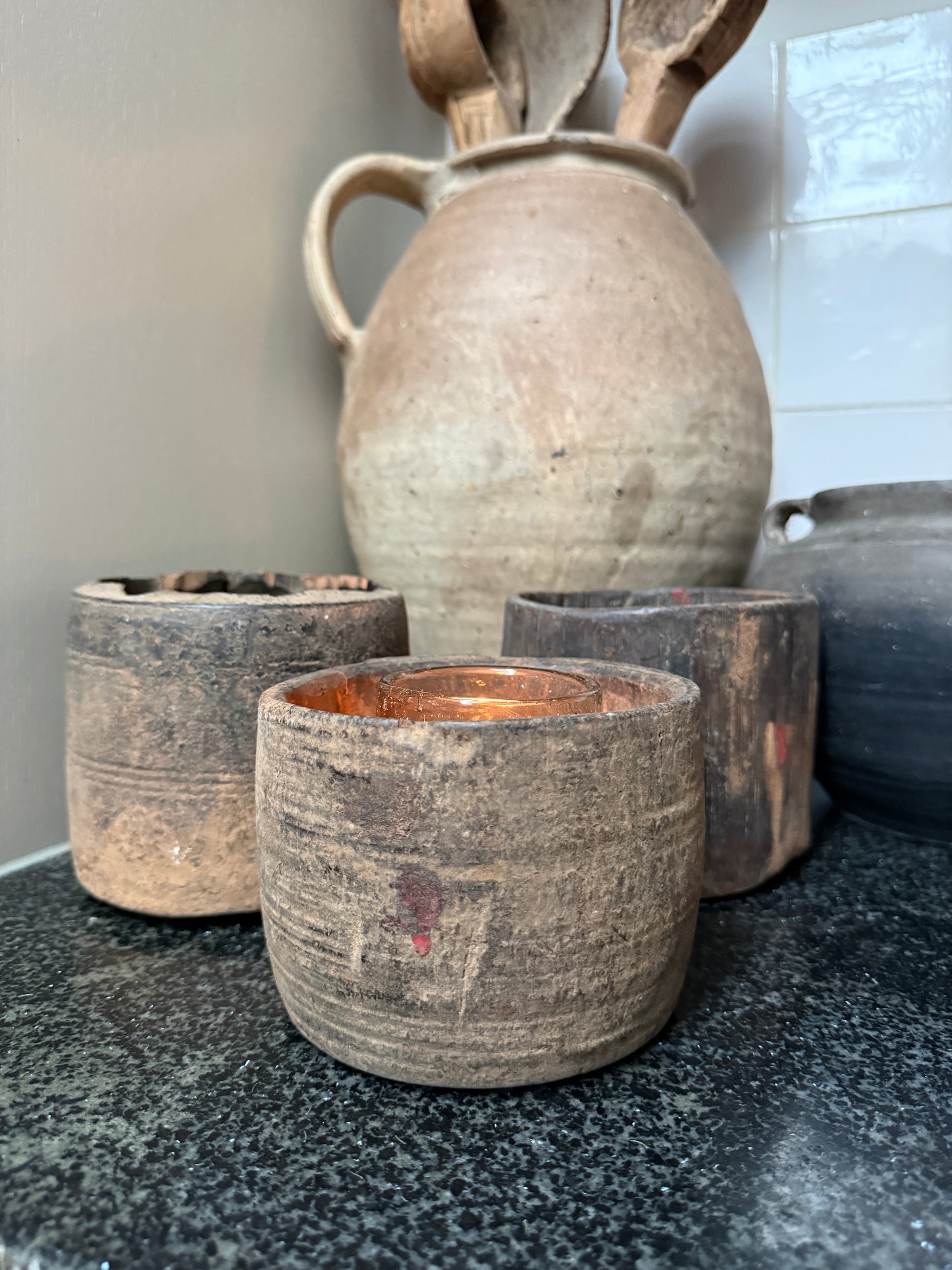 Handgemaakte landelijke woonaccessoires, ruwe houten potjes en aardewerken kruik op een stenen blad