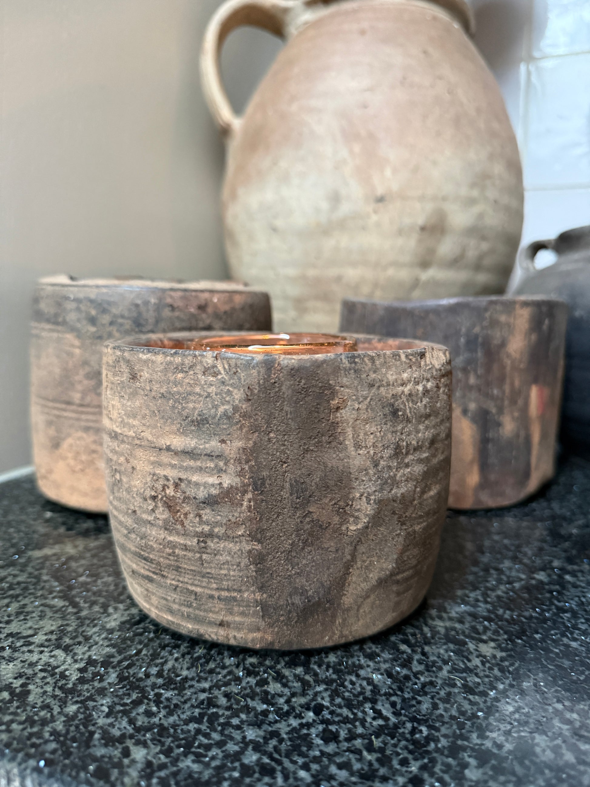 Handgemaakte houten theelichthouder en kruik op zwart blad, sober landelijk interieur