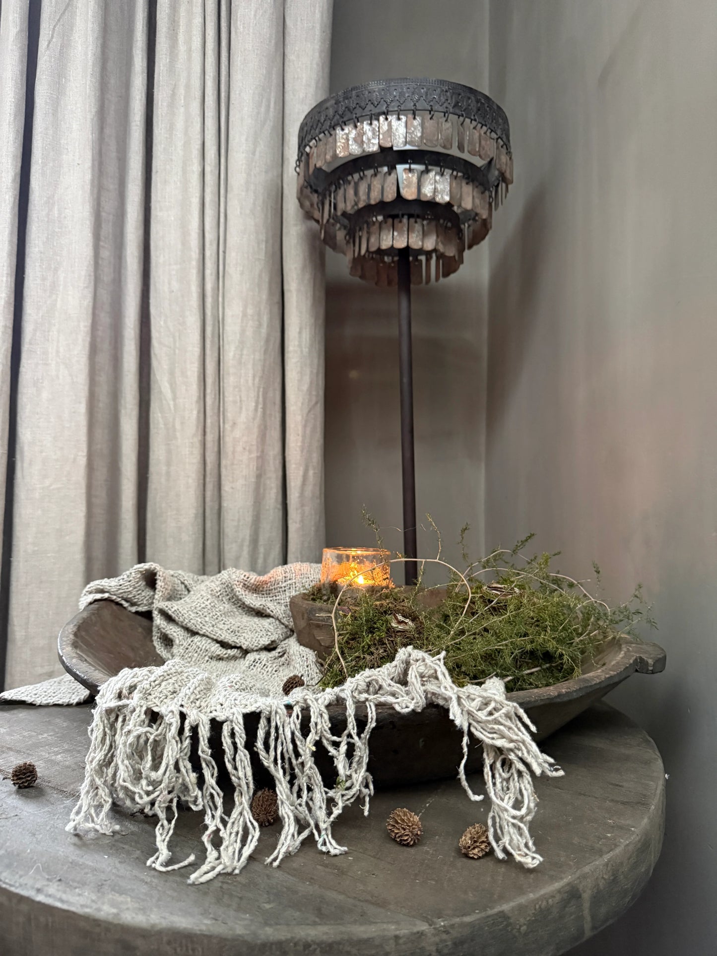 Sober, landelijke woonaccessoires met houten schaal, linnen doek en brandend windlicht op tafel