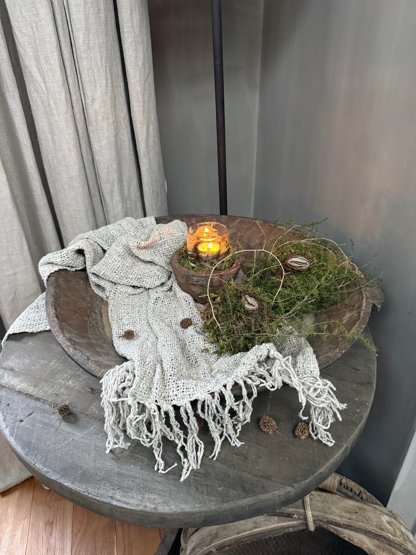 Sober landelijke decoratie met handgemaakt kleed, houten schaal, kaars en mos op ronde tafel