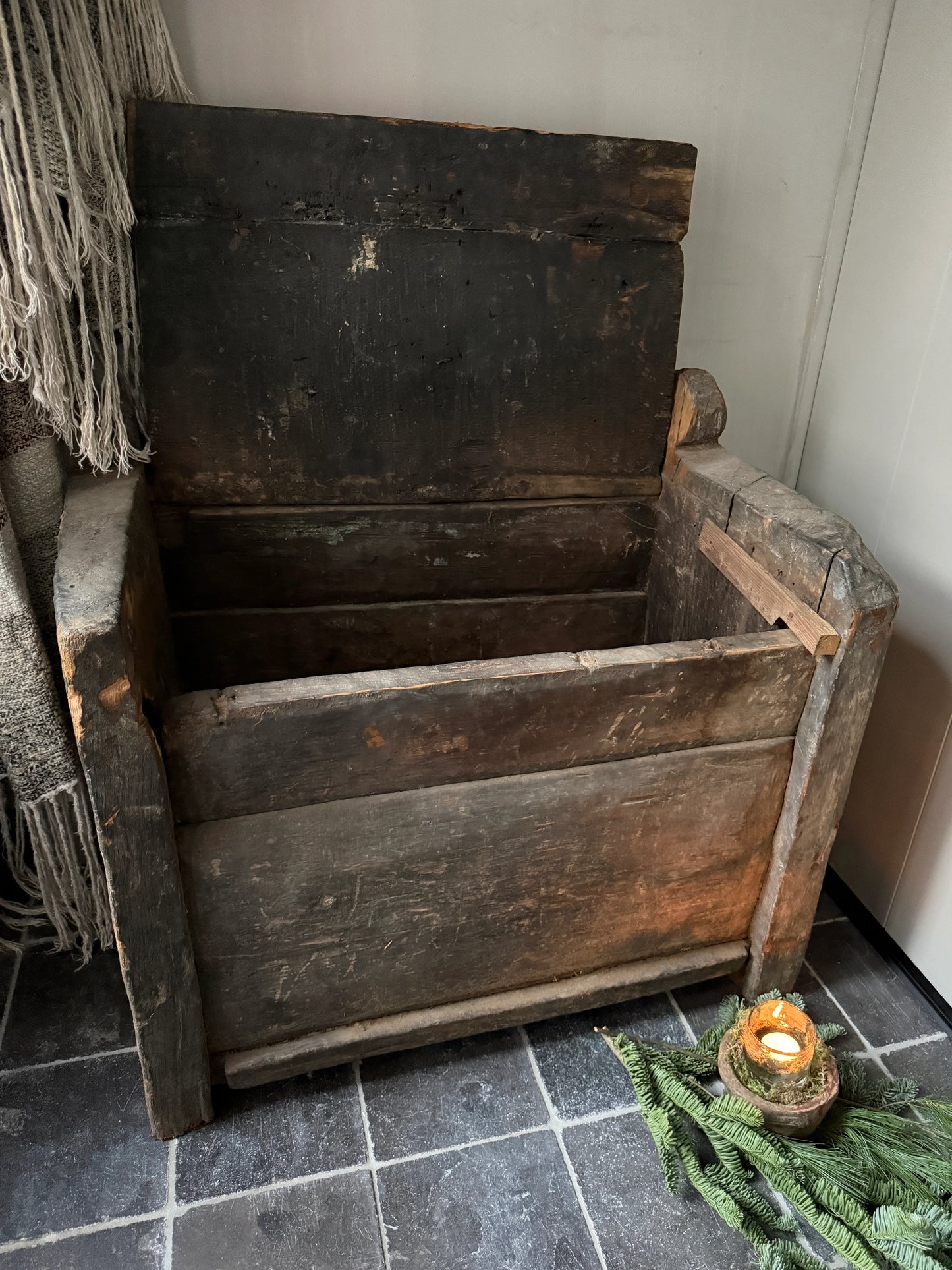 Authentieke, handgemaakte houten kist met sobere landelijke uitstraling, naast kaarsje en dennengroen.