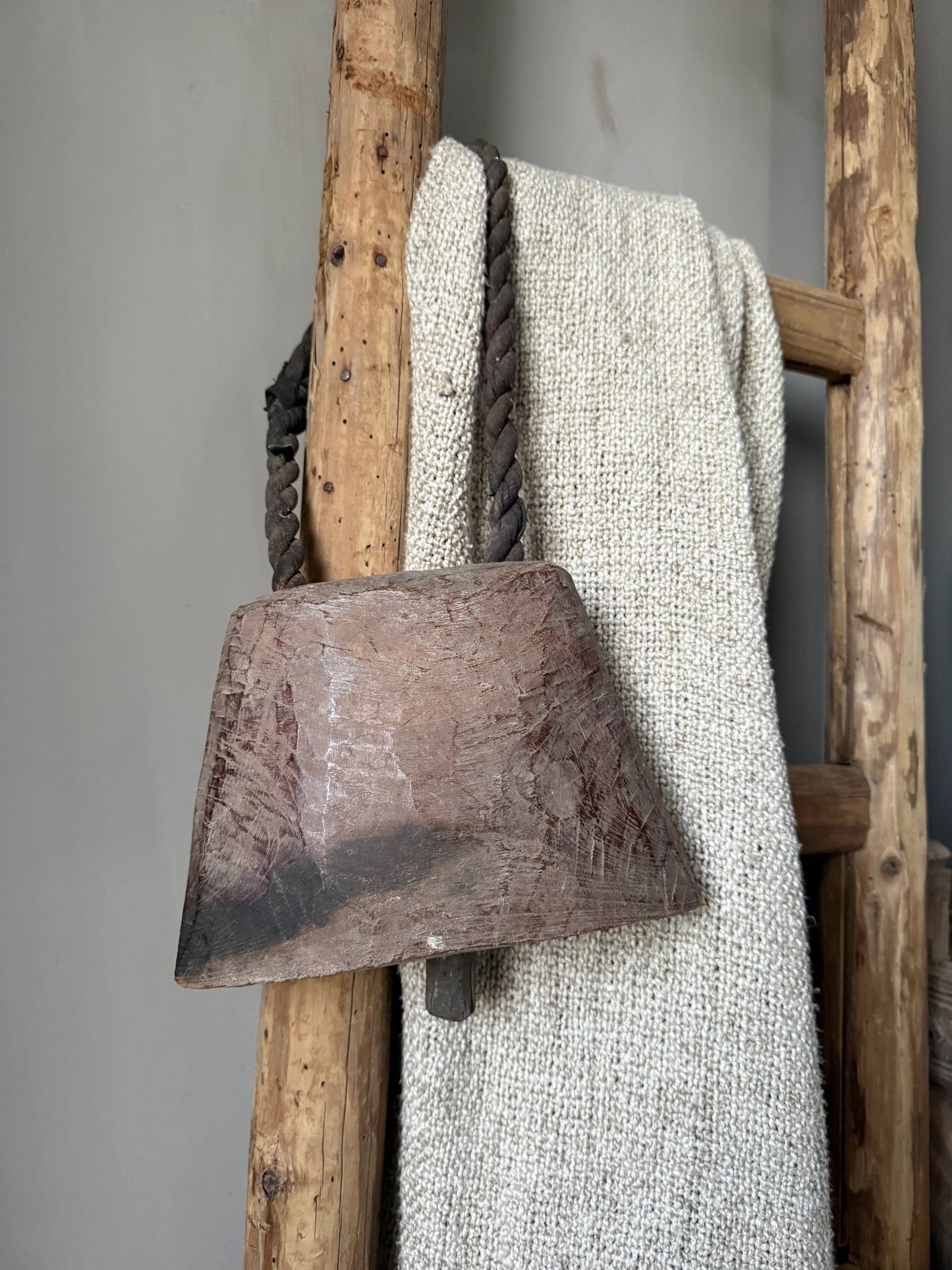 Handgemaakte houten bel aan rustieke ladder met beige plaid, sober landelijk interieur