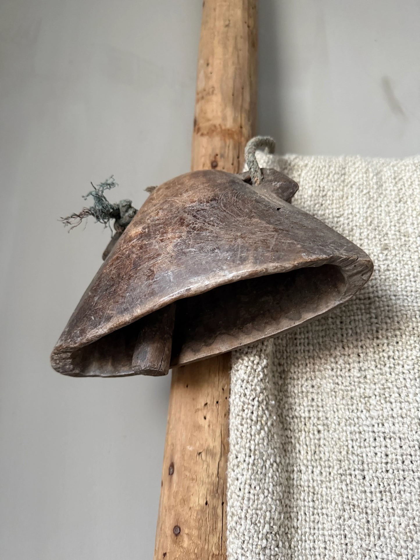 Authentieke handgesmede metalen bel aan houten paal, sober landelijk interieur