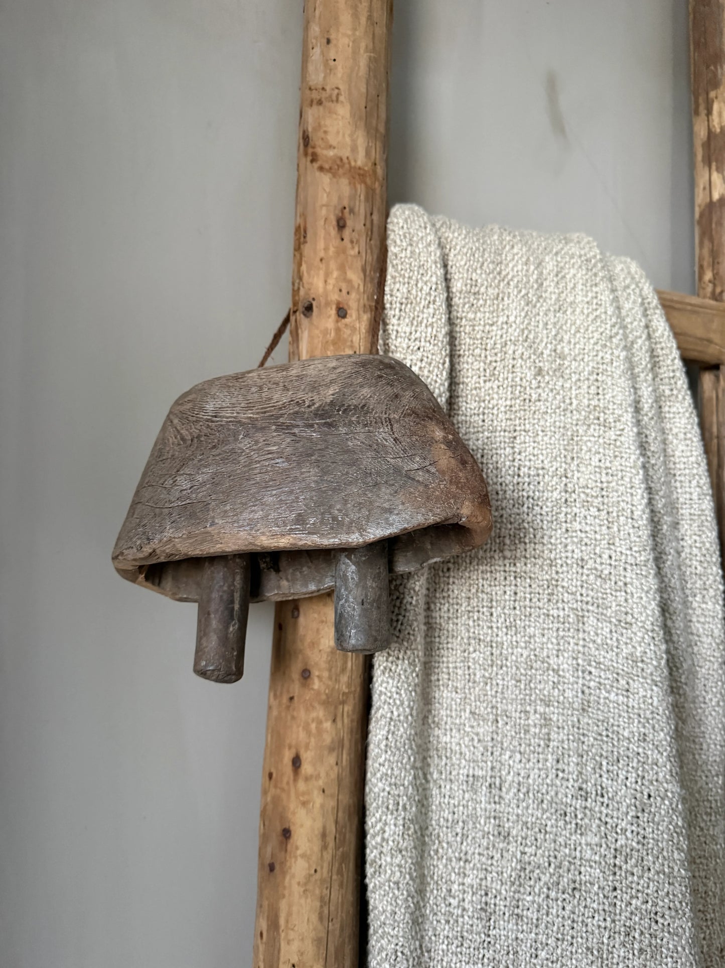 Handgemaakte houten bel aan rustieke ladder met grof gebreid plaid, landelijk interieur