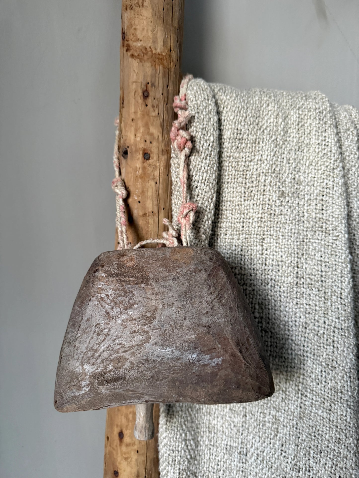 Authentieke handgemaakte bel en grof geweven plaid aan houten ladder, sober interieur