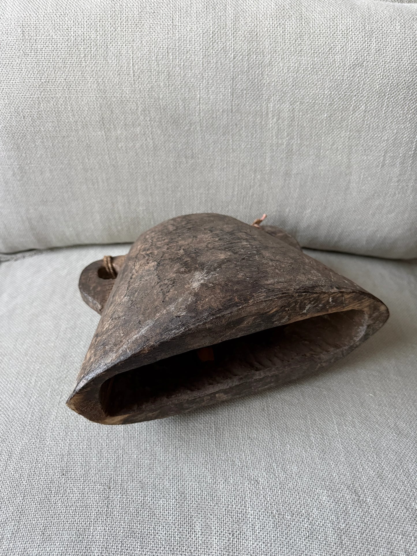 Handgemaakte houten bel uit India, sober landelijk woonaccessoire op lichtgrijze stof