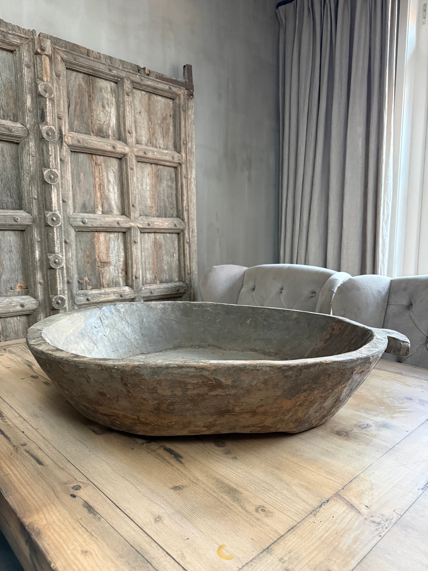 Handgemaakte houten schaal op rustieke tafel in sober landelijk interieur met oude deur