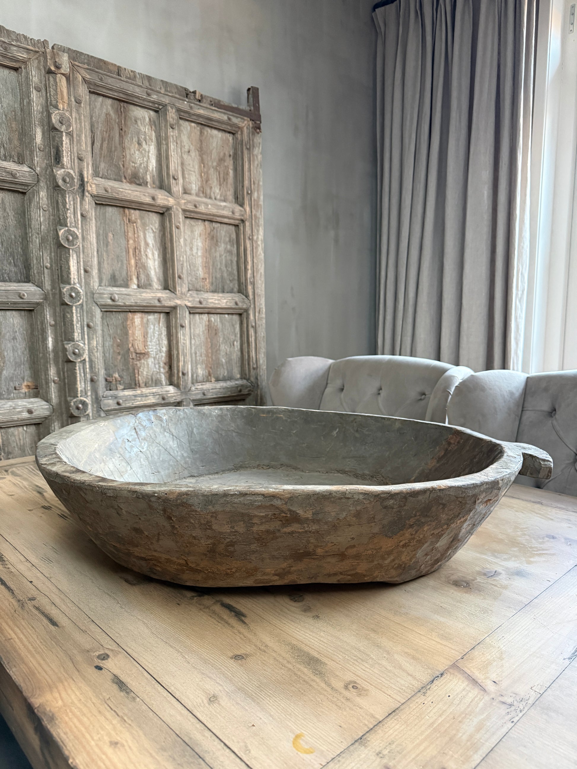 Handgemaakte houten schaal op rustieke tafel in sober landelijk interieur met oude deur