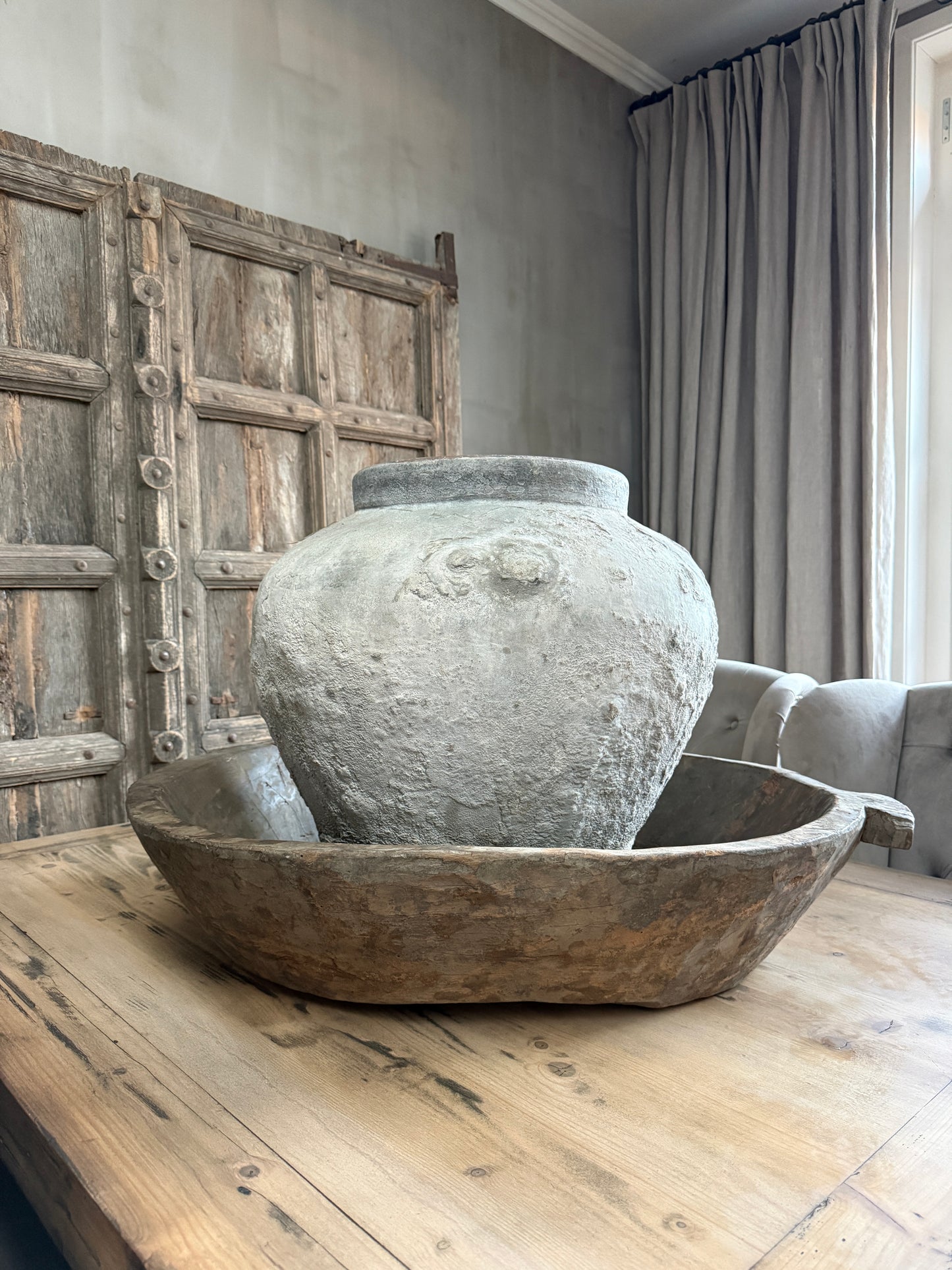 Authentieke, handgemaakte grijze kruik in houten schaal op landelijke houten tafel, sober interieur