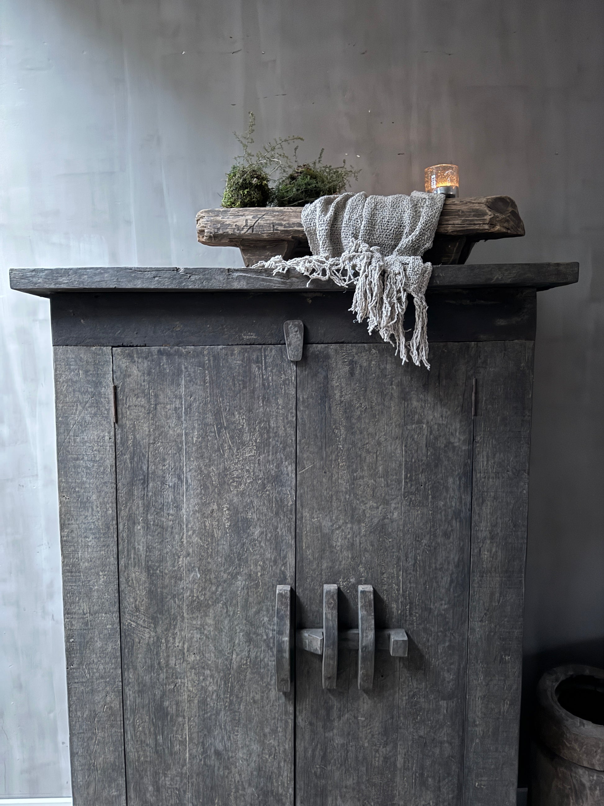 Authentieke grijze houten kast met landelijke decoratie, kaars en plaid, sober interieurstijl