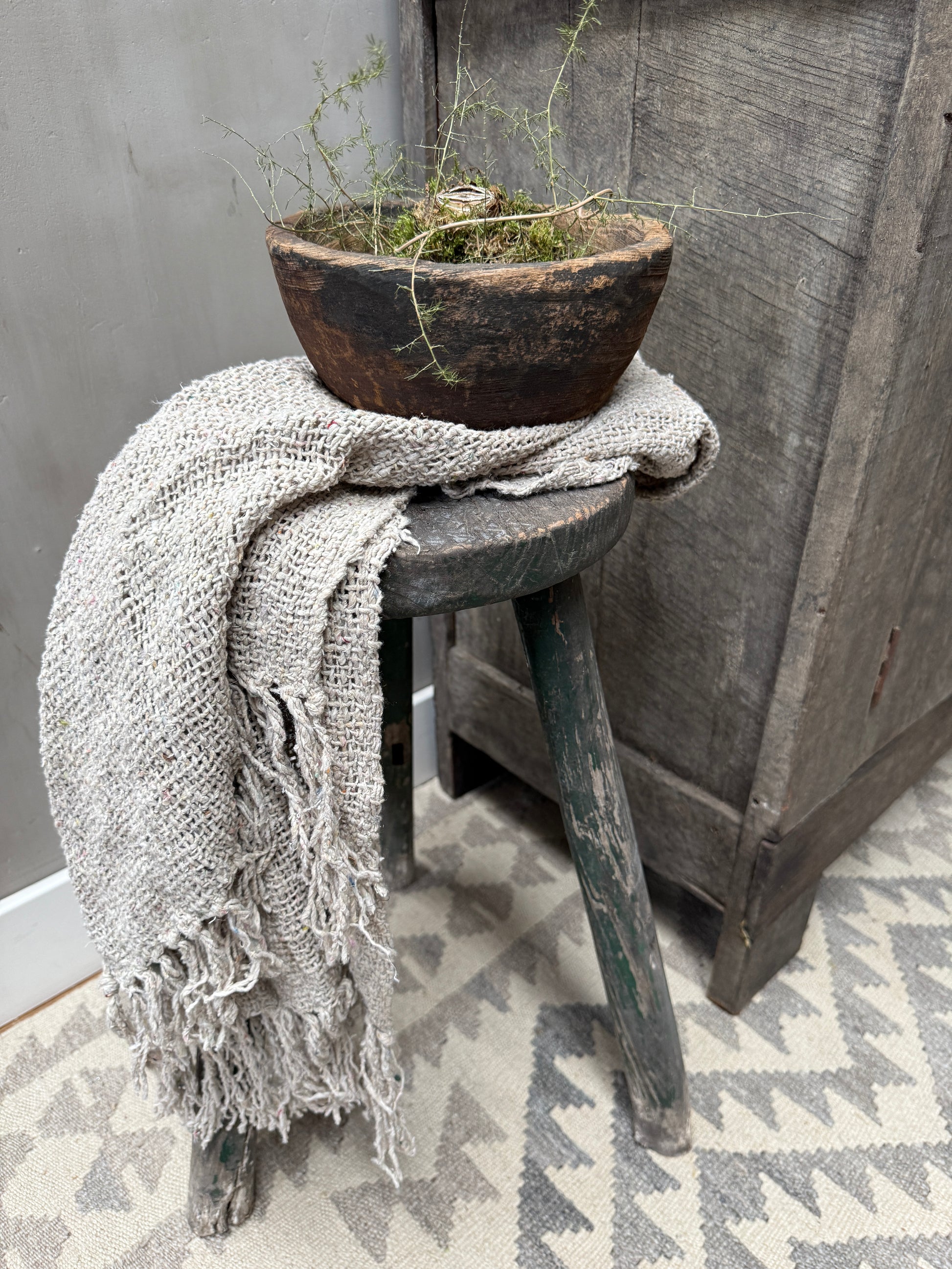 Handgemaakte houten schaal met plant, linnen plaid op vintage kruk, sober landelijk interieur